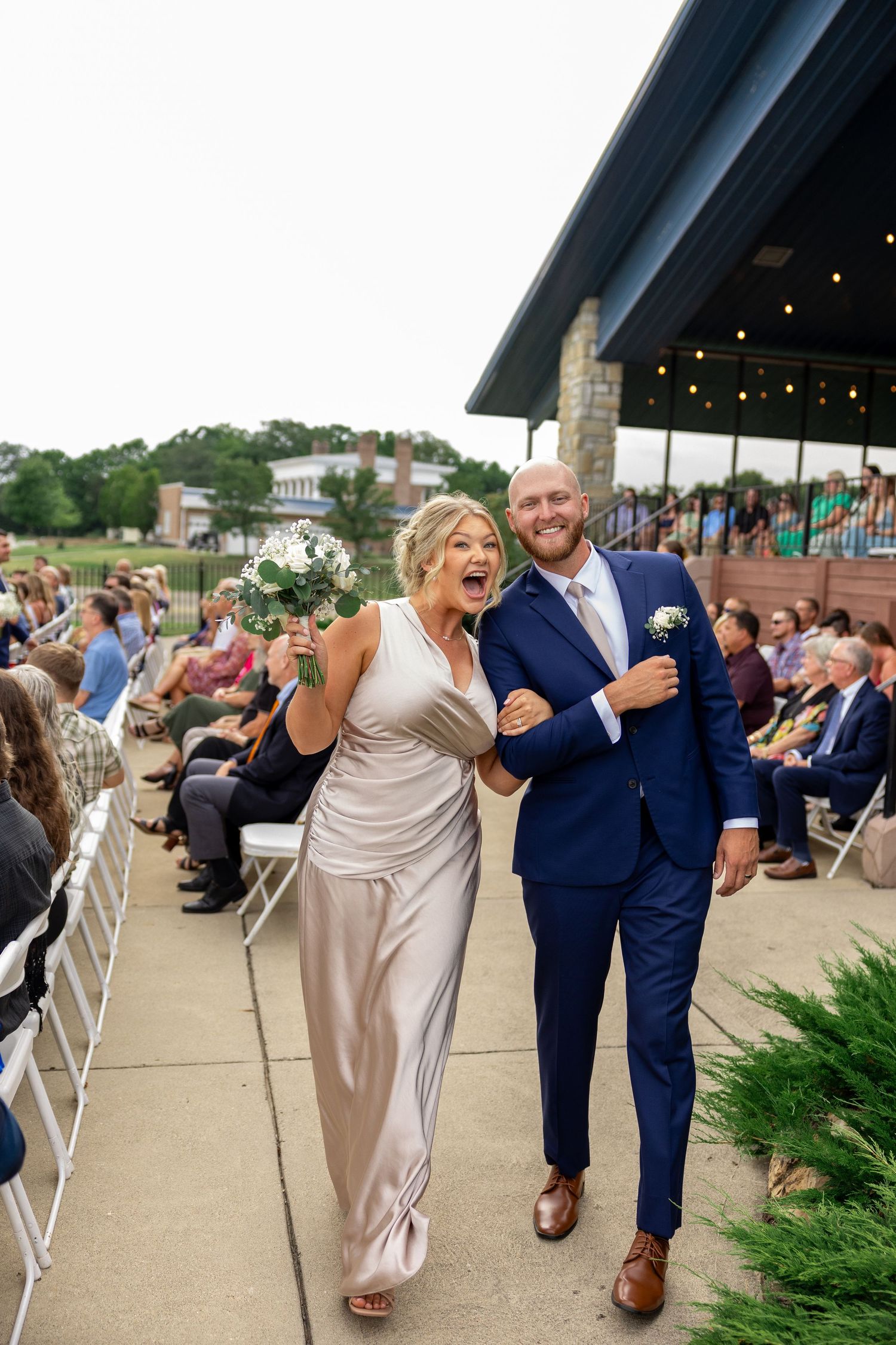 Wedding party walking and celebrating on outdoor patio in blue suits and neutral dresses.