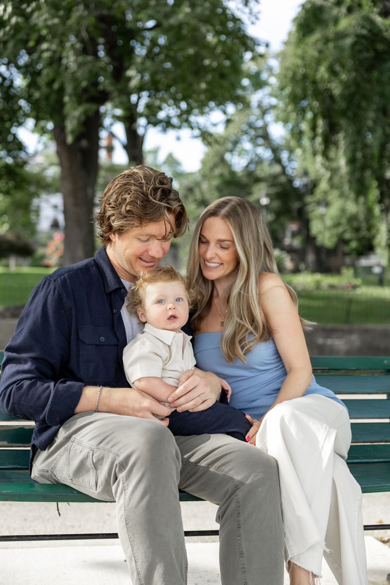 Family sharing tender moments while sitting on park bench near water.