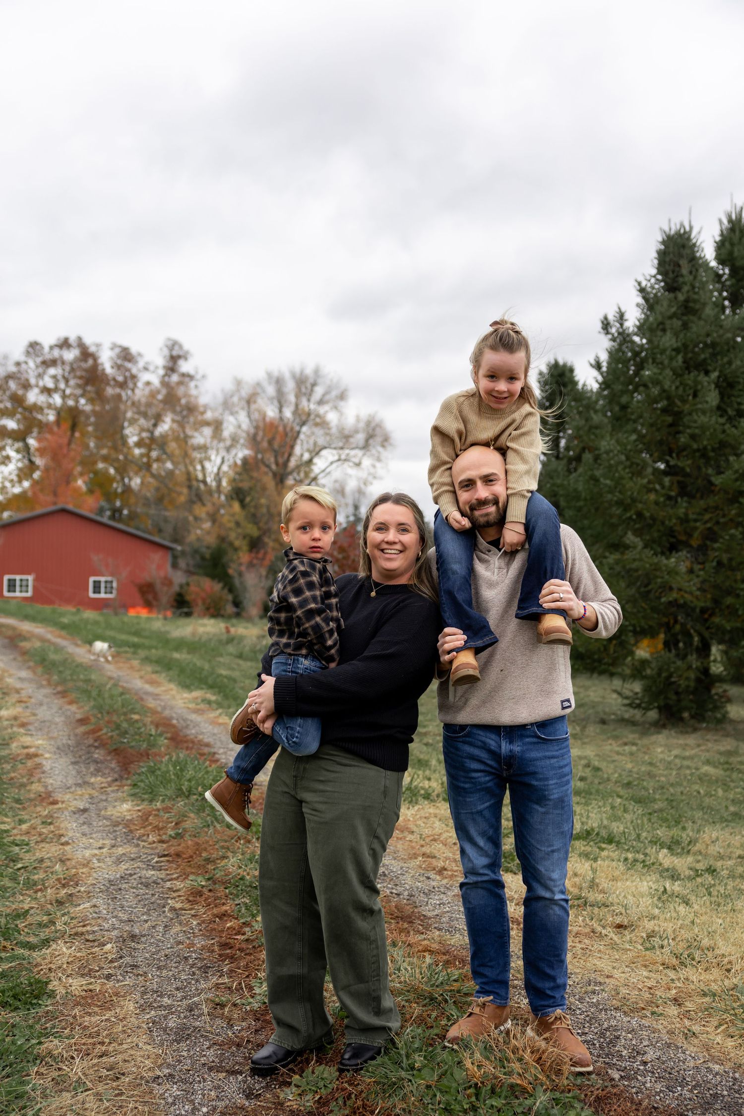 Family enjoying a playful moment on a path near a Christmas tree farm.