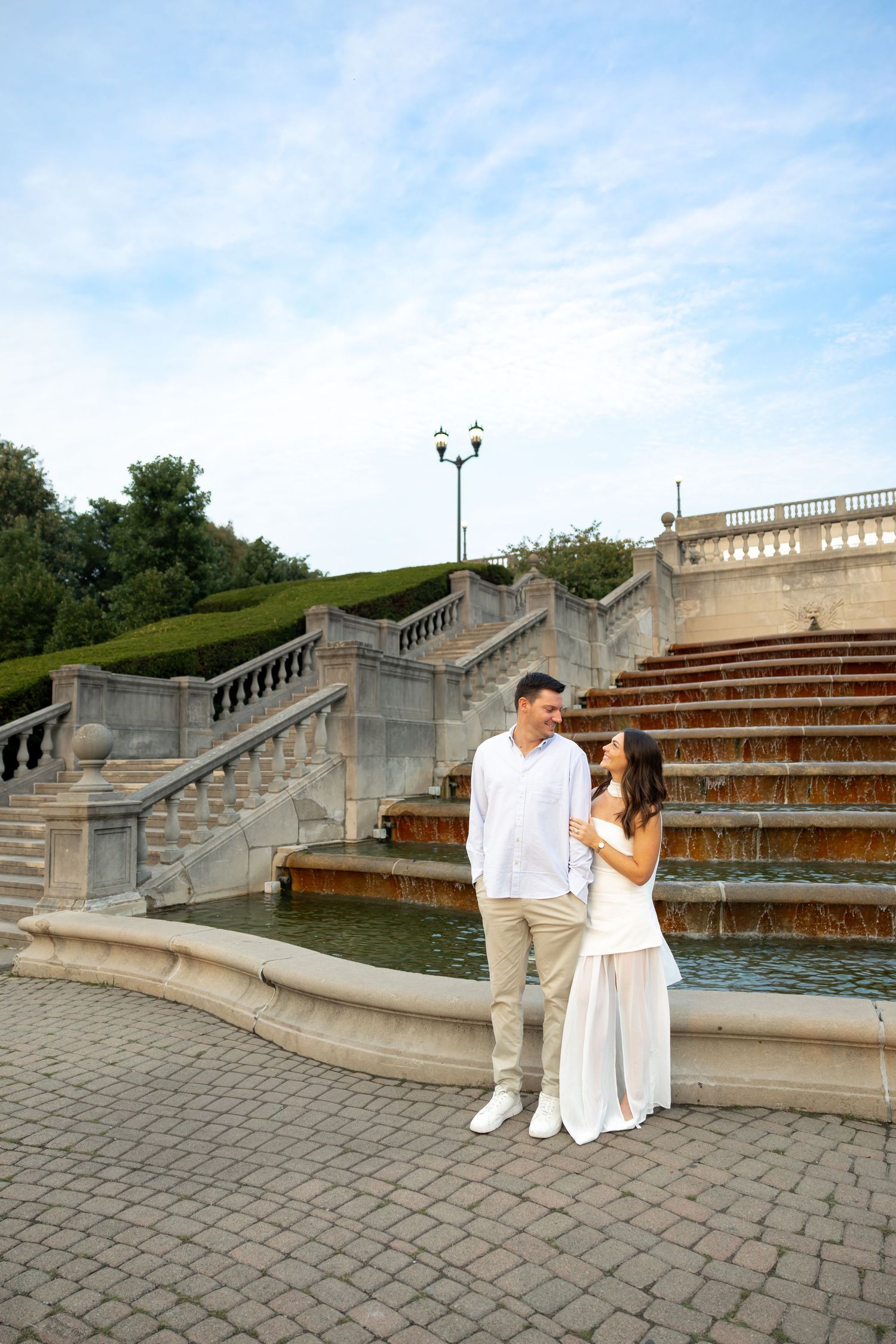 A romantic photoshoot on stone steps with white balustrades against a cloudy sky.