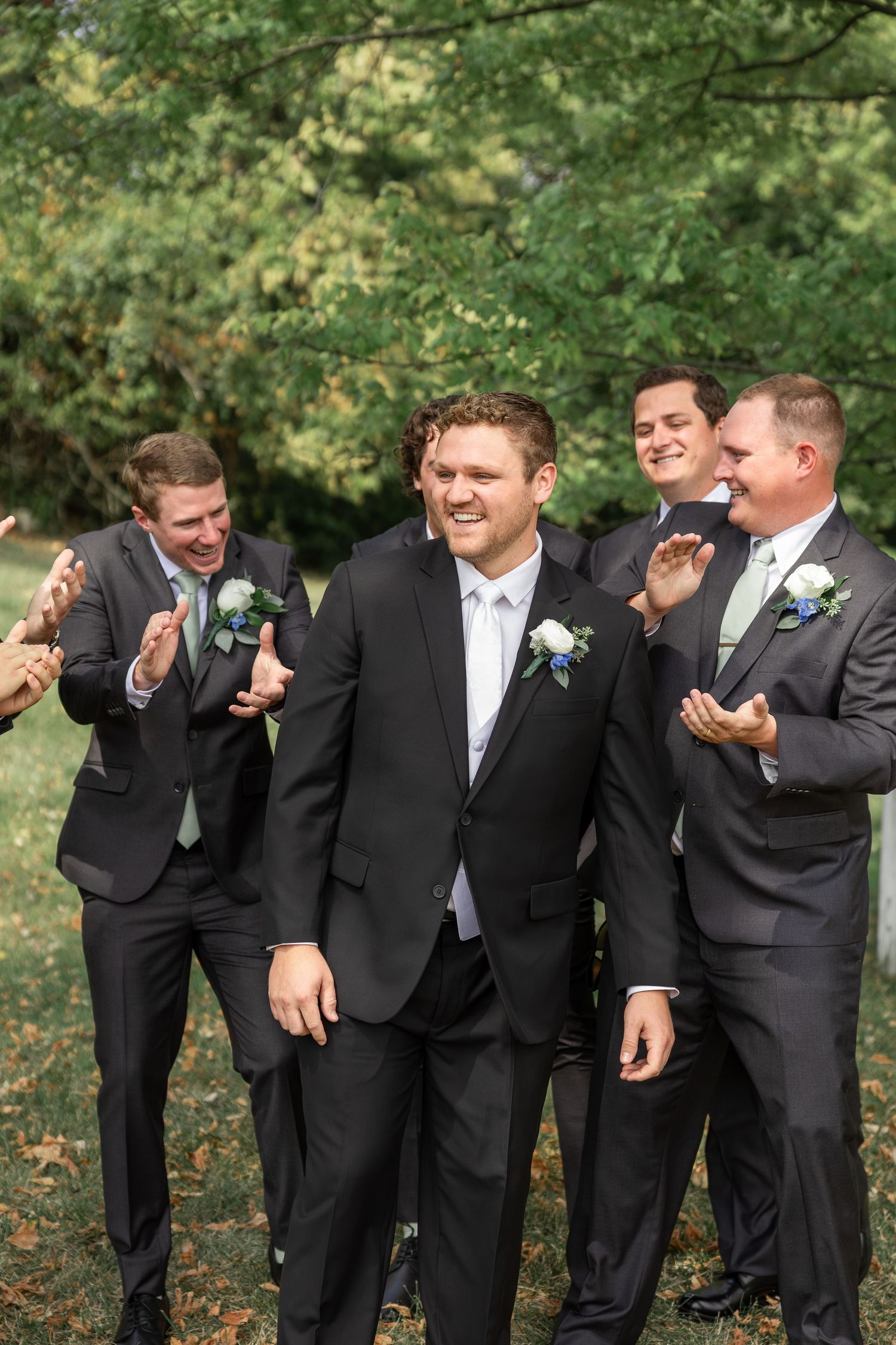 Groomsmen in black tuxedos sharing laughs during outdoor wedding photos.