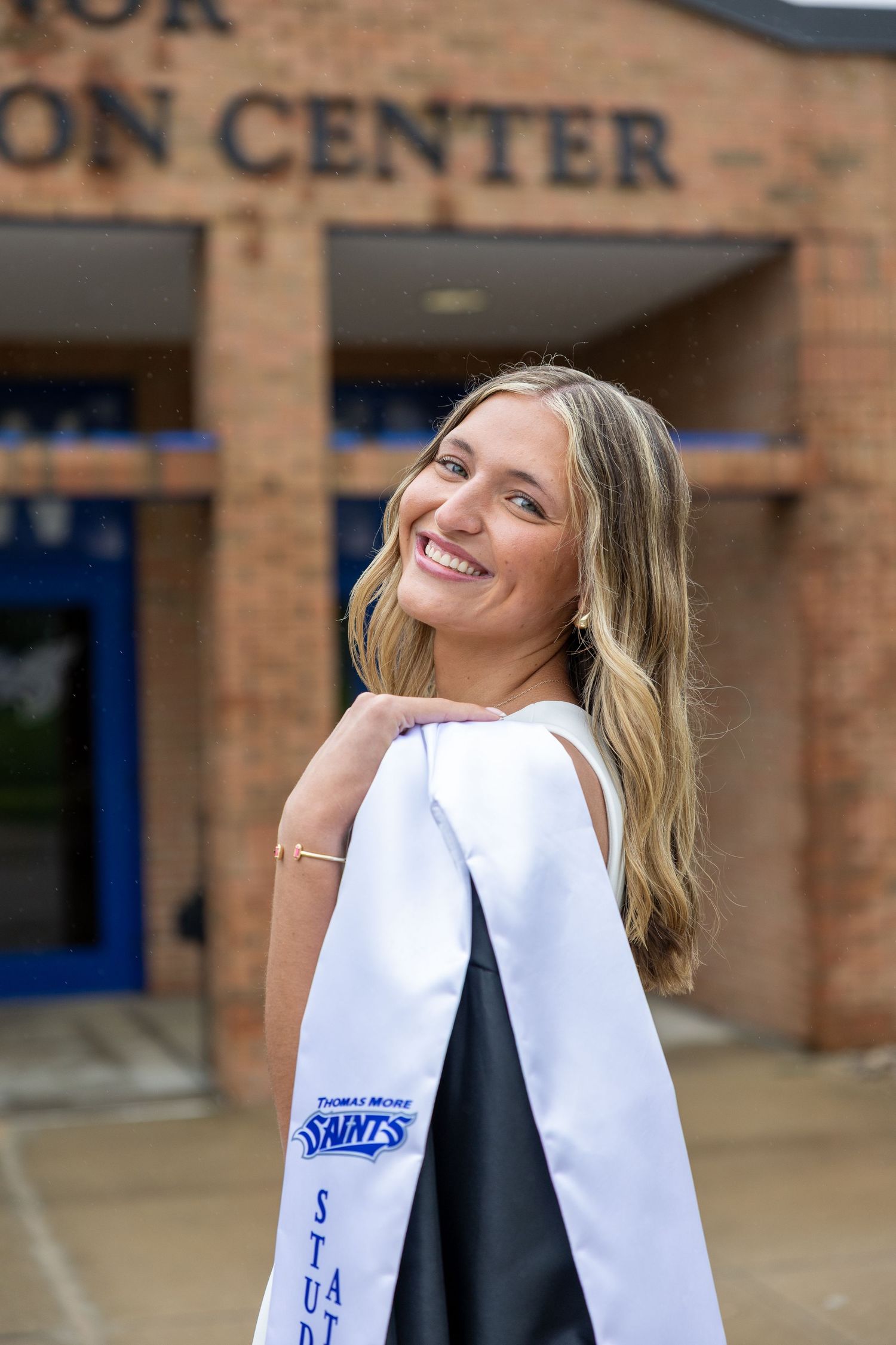 Graduate celebrating with graduation gown and Snakes team spirit wear outside brick building.
