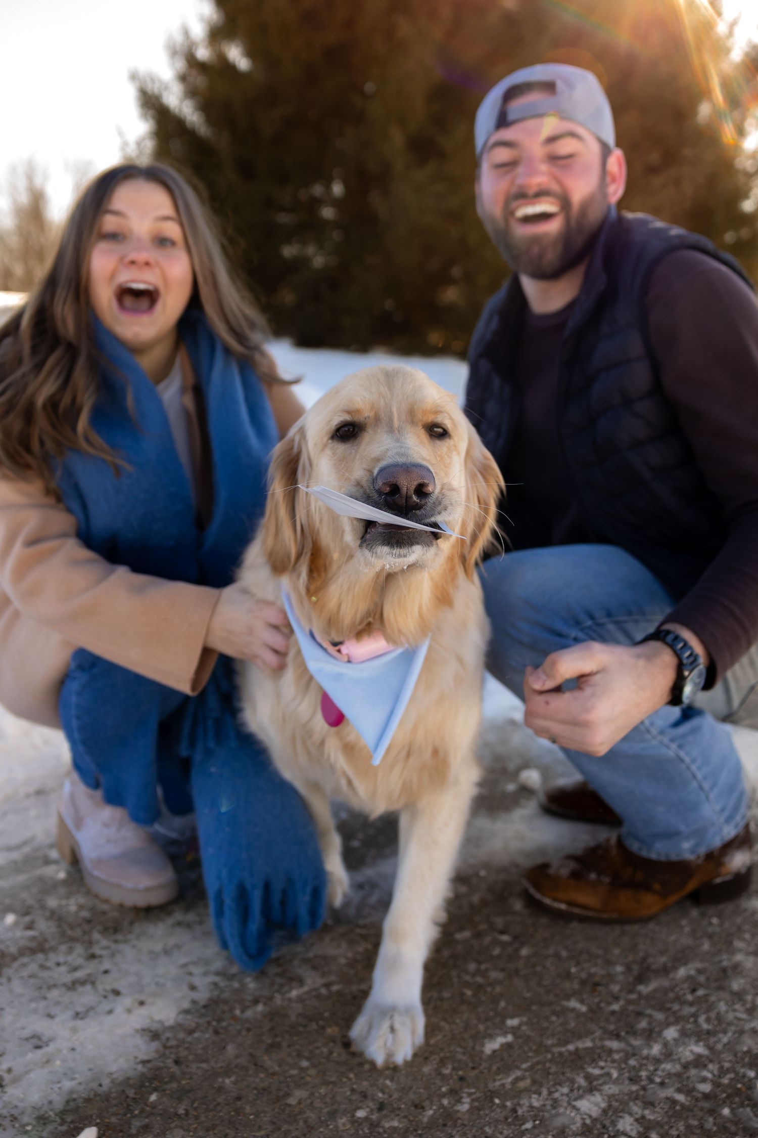 Happy couple taking playful photos with their golden retriever dog outdoors at sunset.