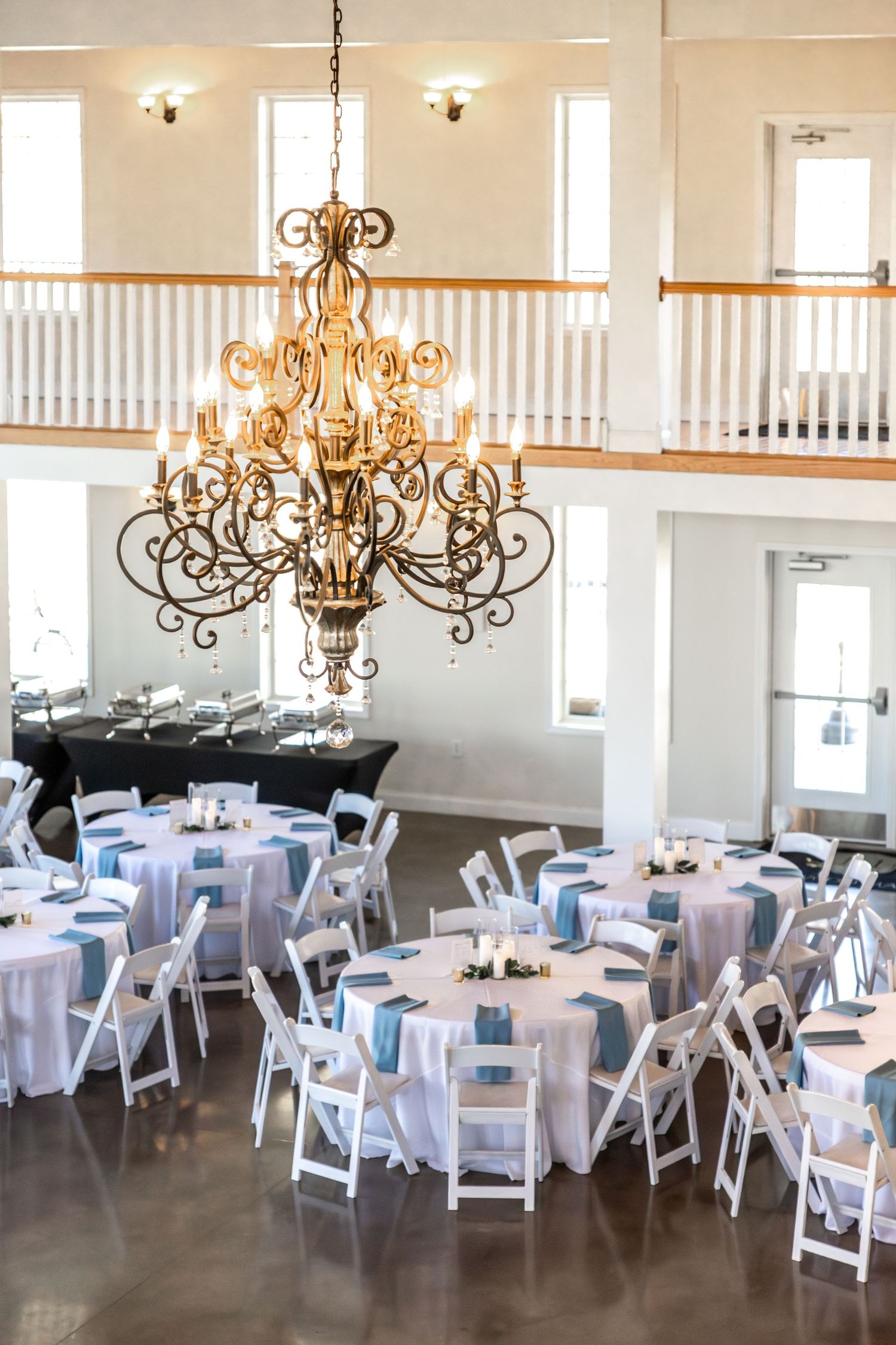 Elegant wedding reception venue with white folding chairs, round tables, and ornate chandeliers.