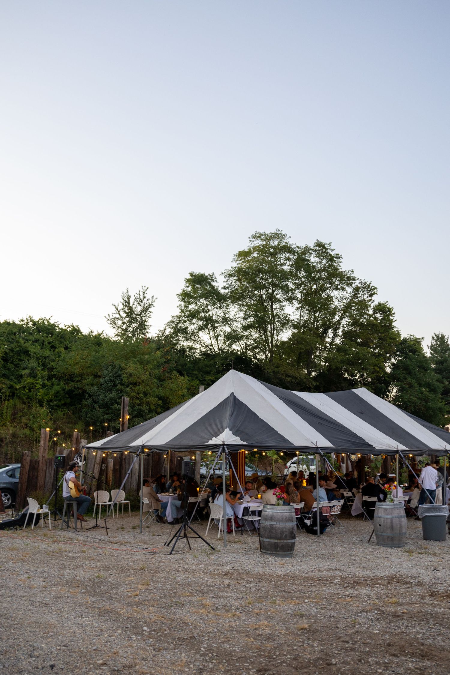 Outdoor event setup with multiple white and black tents at dusk.