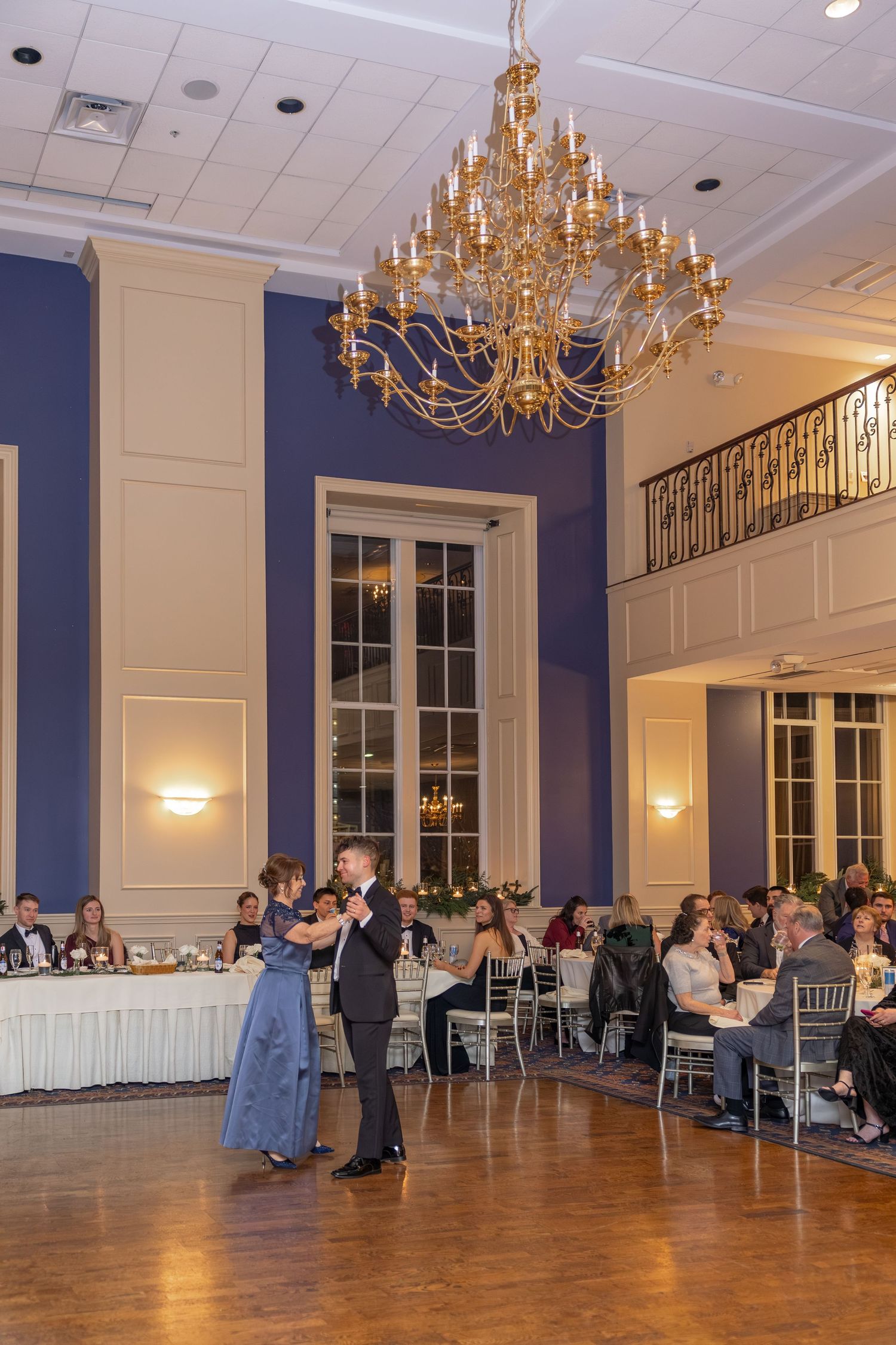 Elegant ballroom with navy walls, chandeliers and wooden dance floor set for a reception.