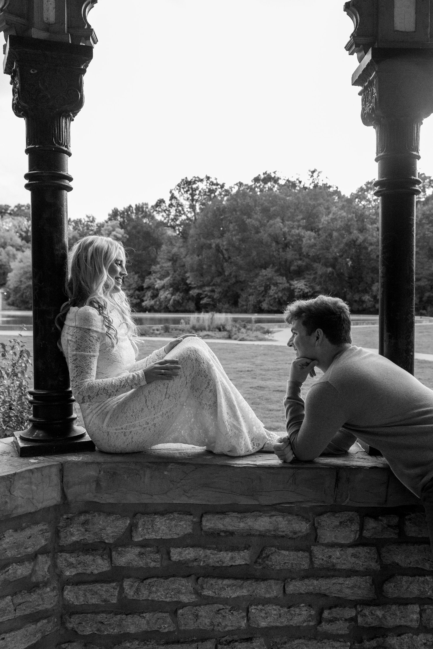 Romantic black and white photo of couple relaxing on stone ledge under archway.