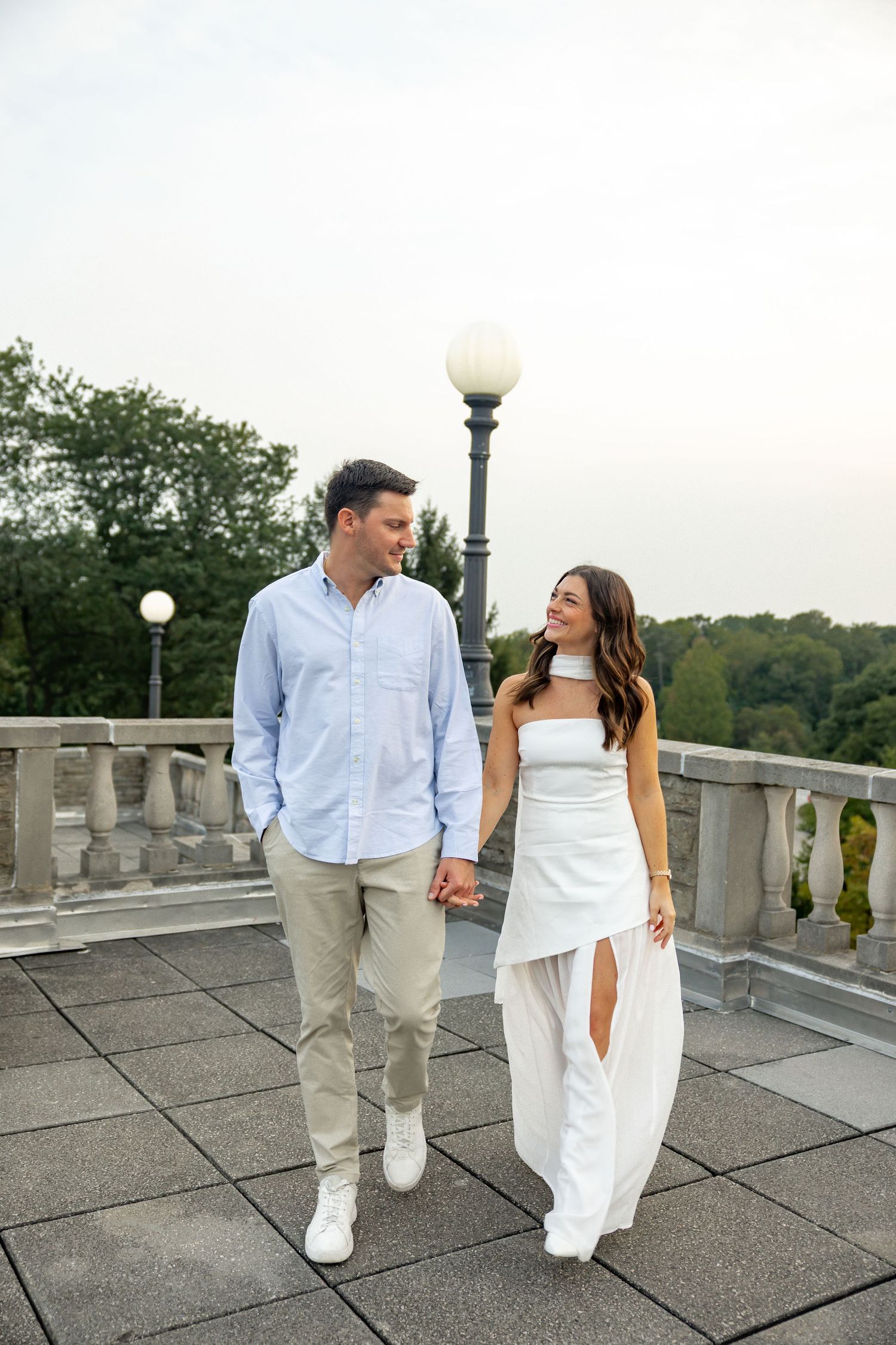 A couple walking and posing together on a stone terrace in coordinated white outfits.
