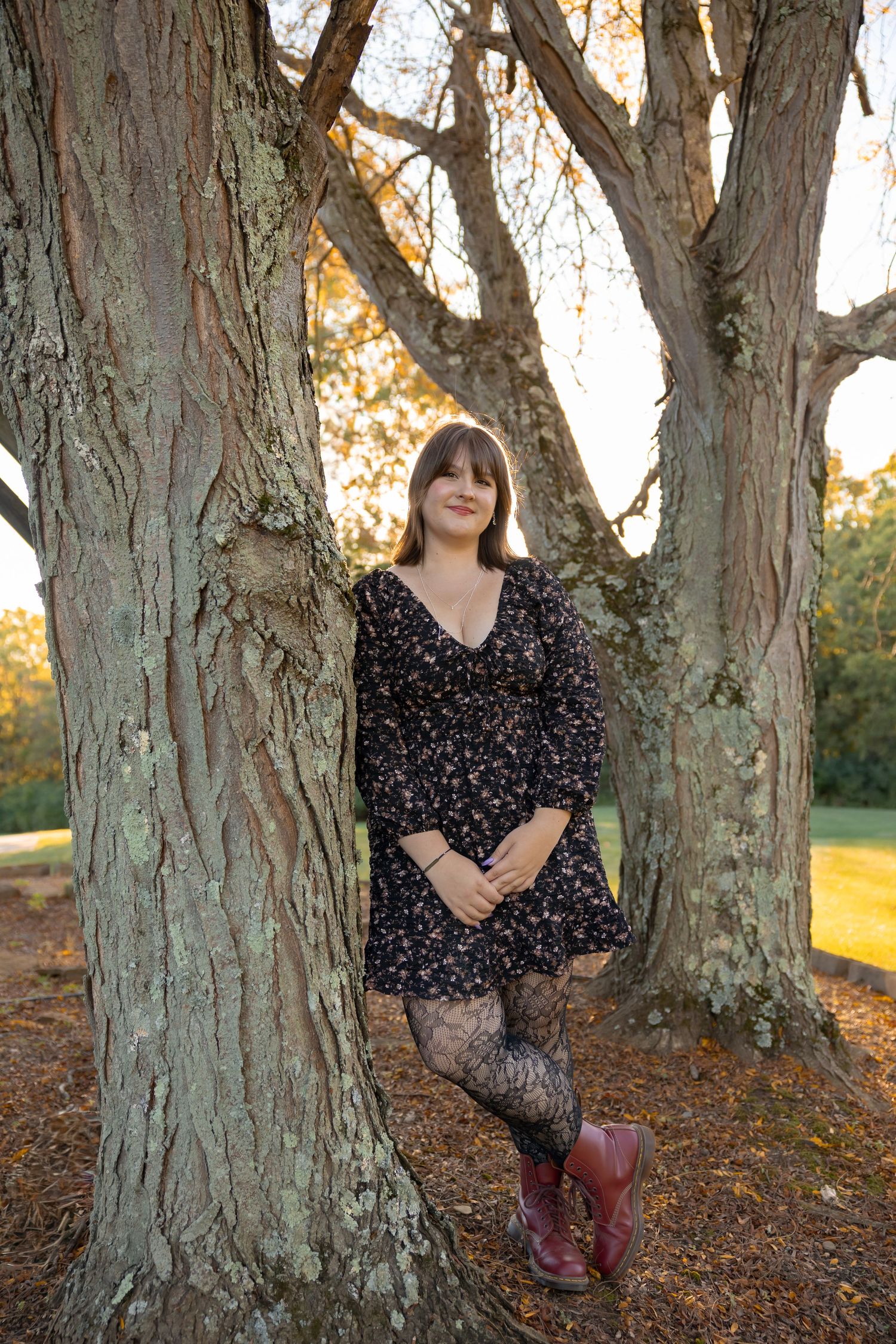 A person in a polka dot dress sits against a large tree trunk during golden hour.