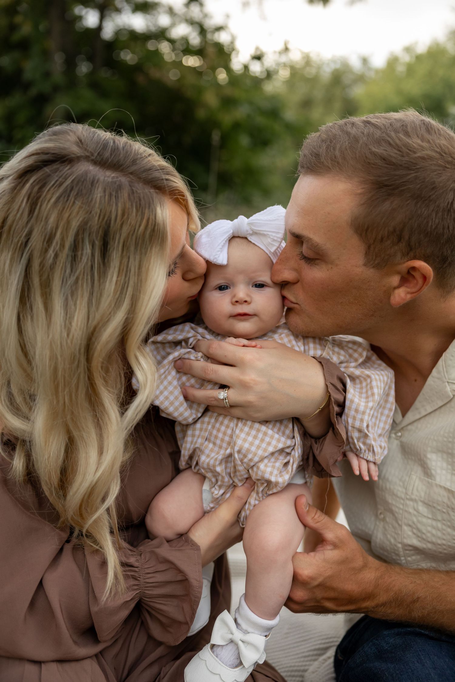A family shares sweet kisses with their baby in warm evening light.