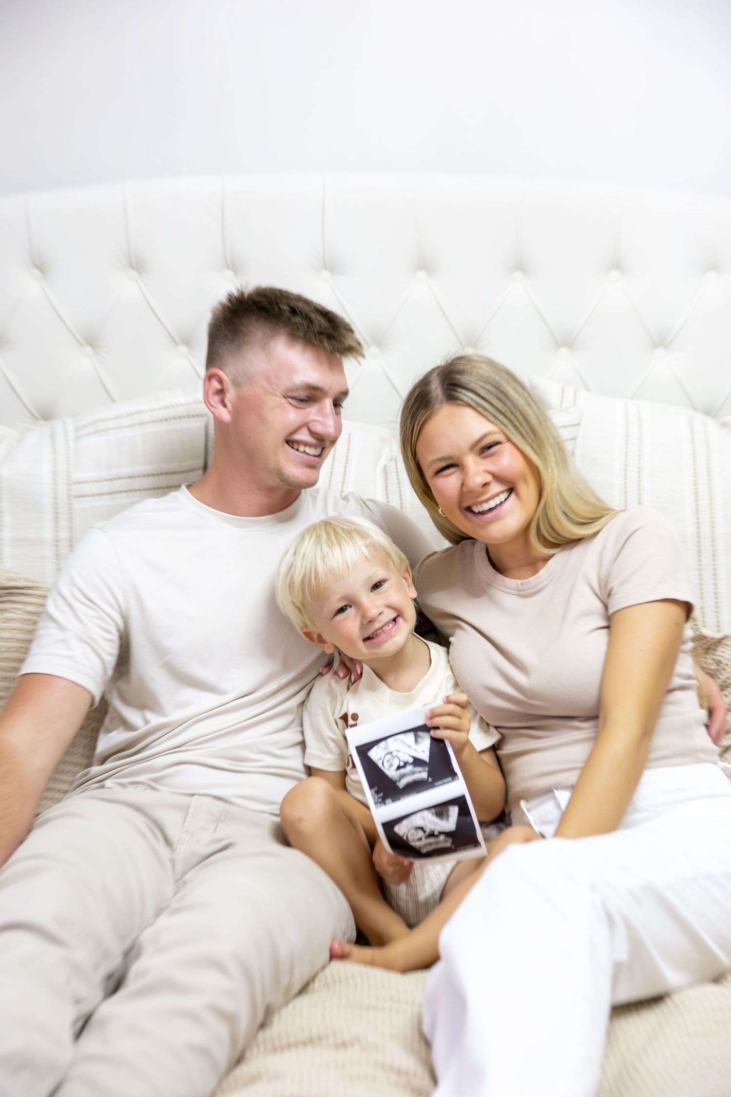Family lounging together on white couch wearing matching casual outfits.