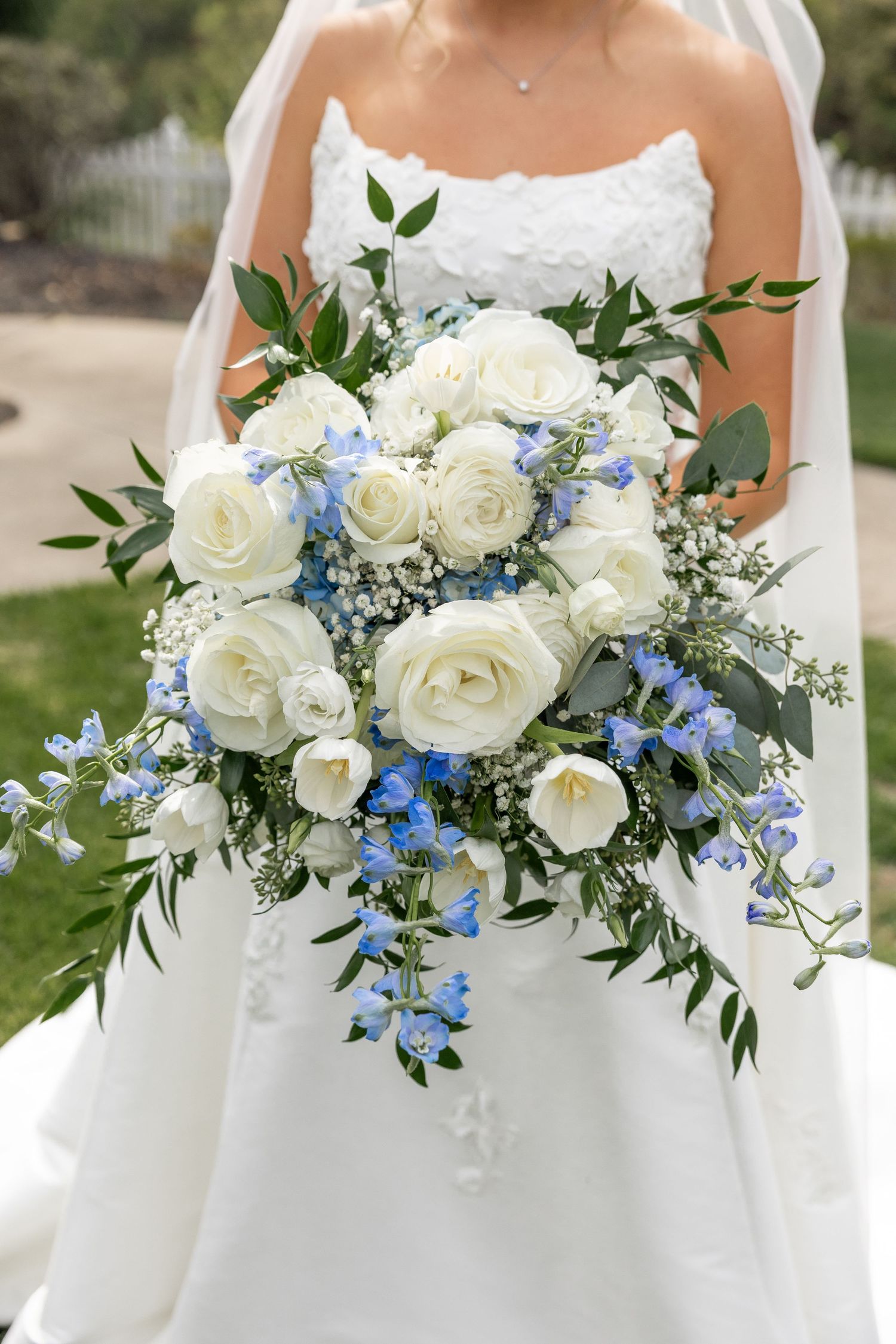 Close-up of bridal bouquet featuring white roses and blue delphinium flowers with greenery.