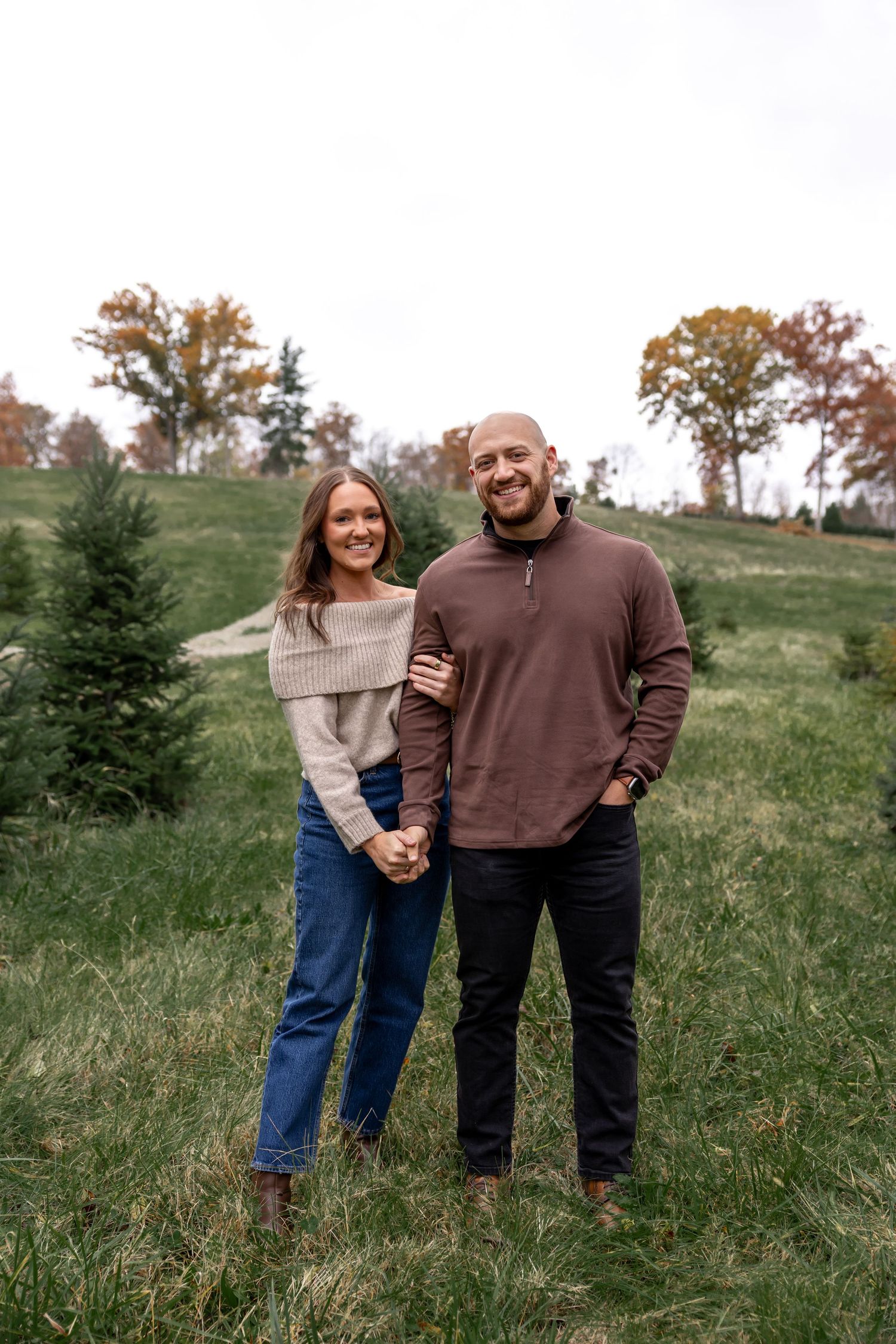 Three people stand together on a grassy hillside during autumn.