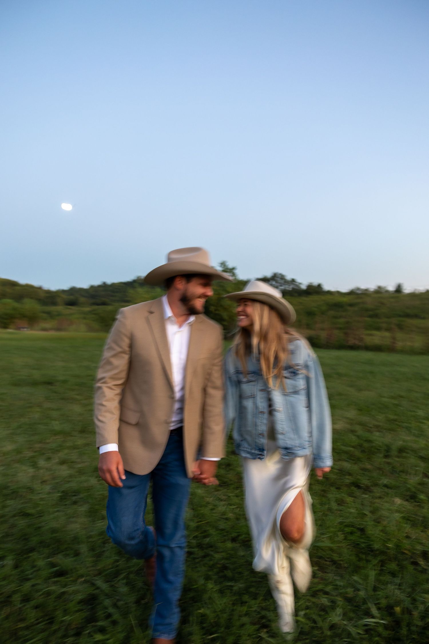 Couple walking through a green field at sunset wearing casual attire.