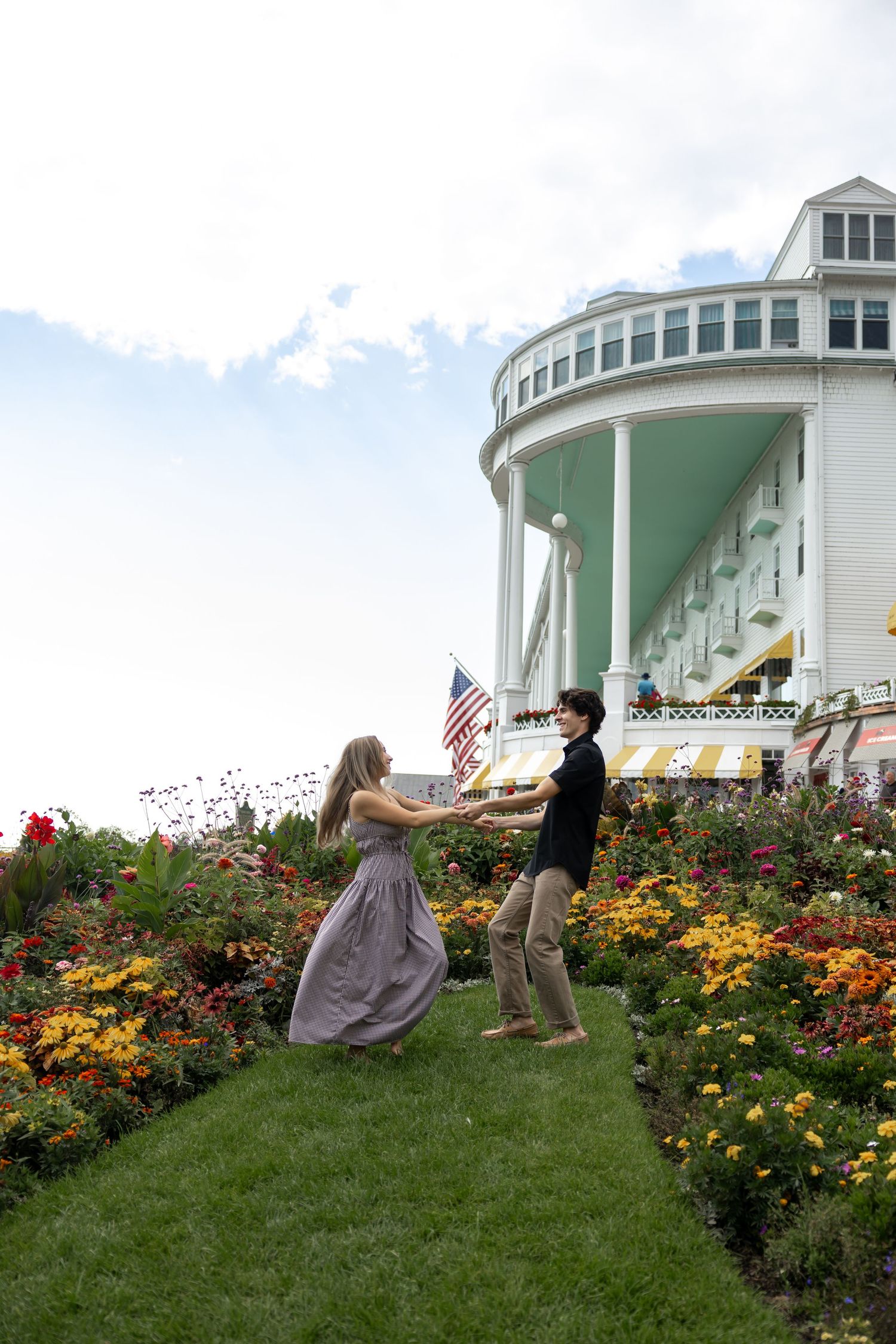 People enjoying a sunny day in a flower garden near a grand white building.