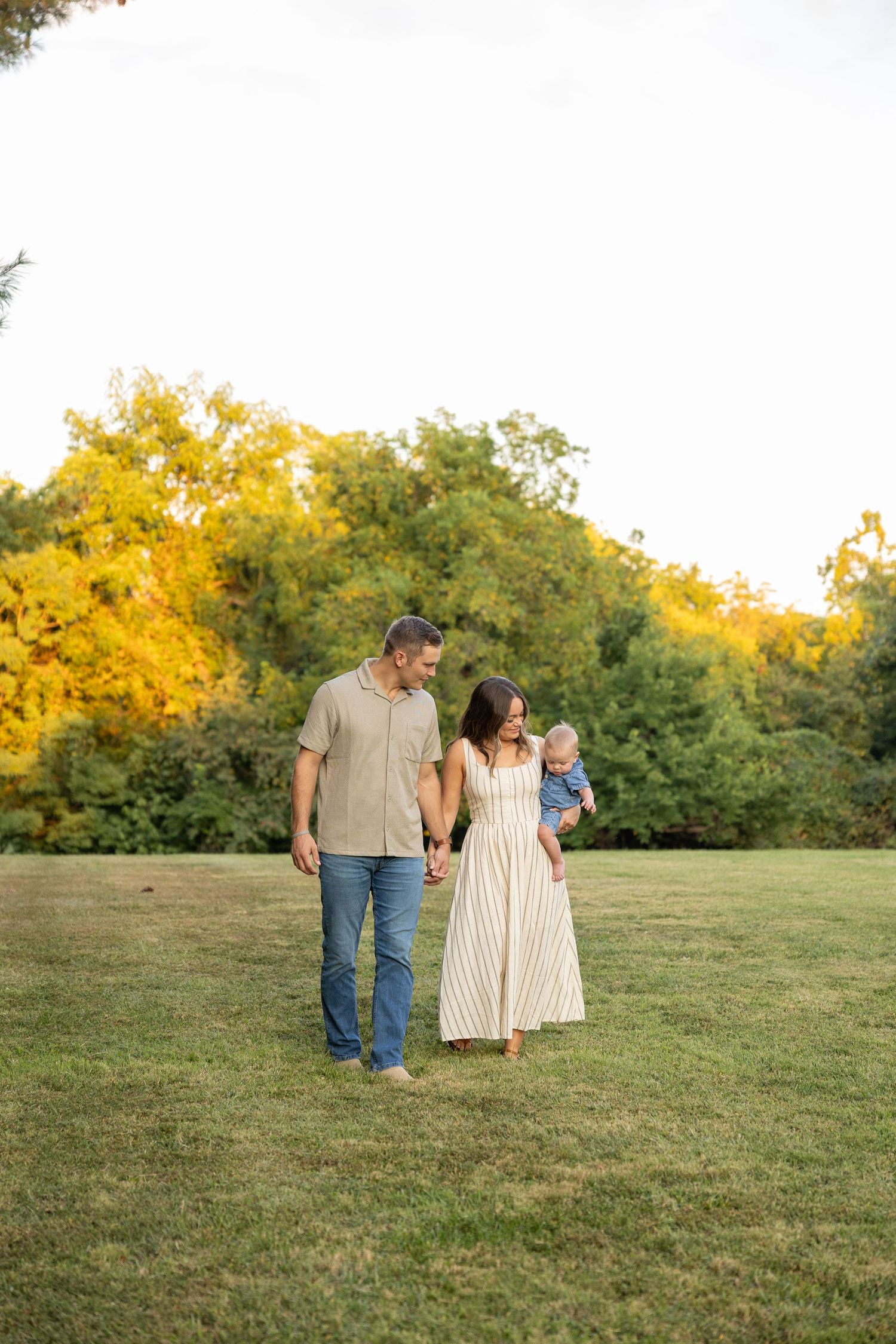 Family walking together through a grassy field at sunset with golden trees in background.