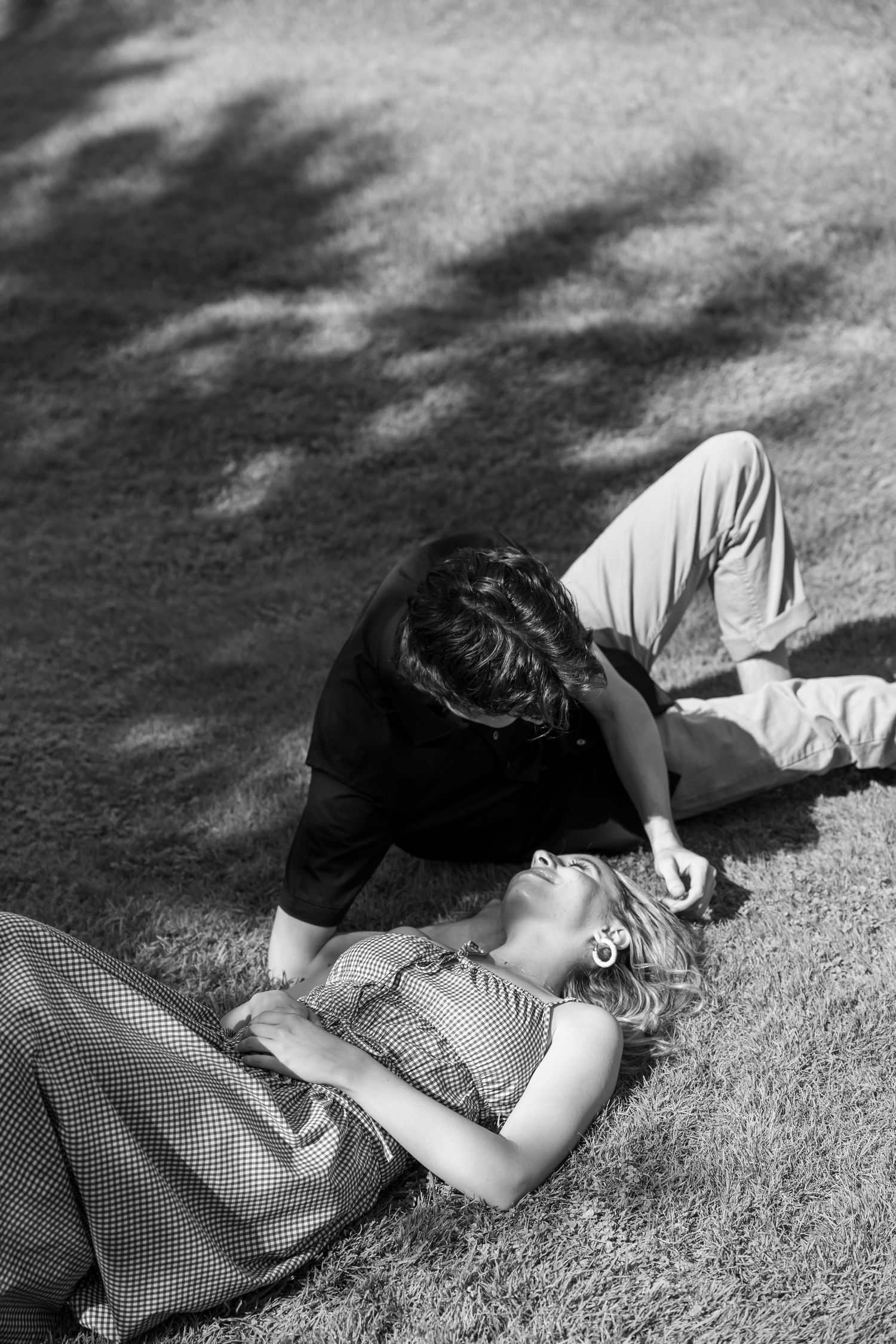Black and white image of two people lying close together in dappled sunlight.