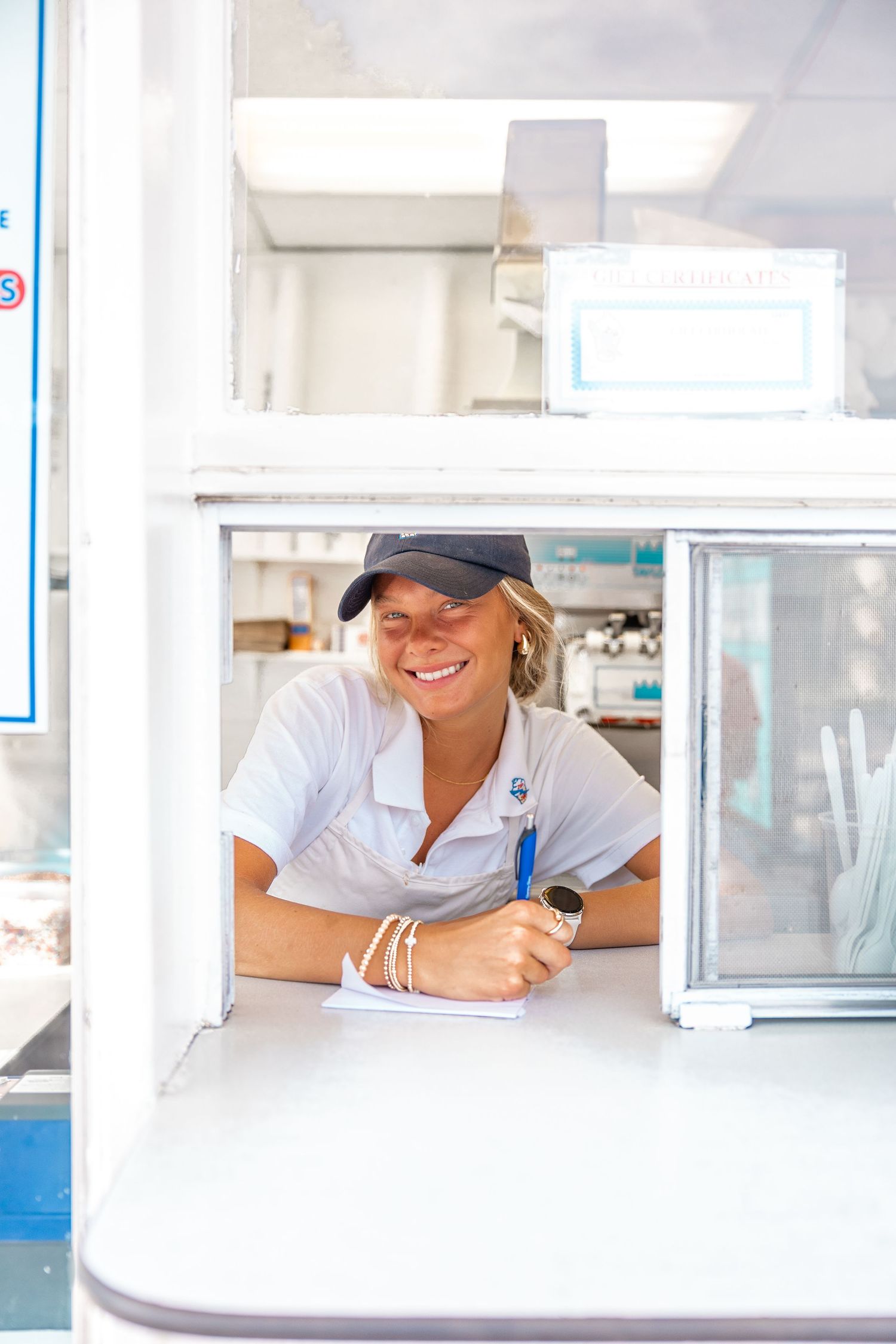 Person in white uniform smiles while working at a service counter window.
