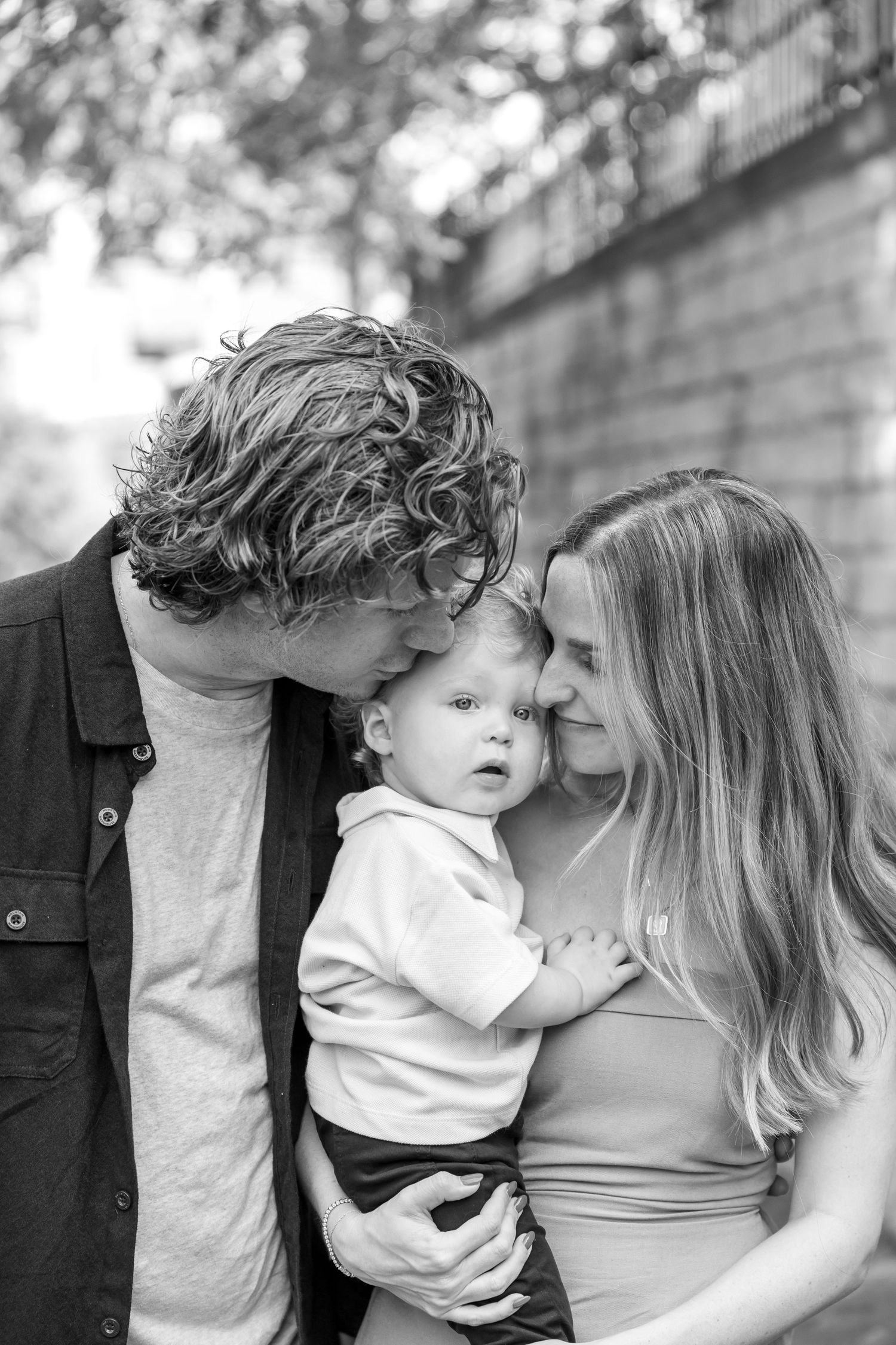 Intimate black and white family portrait captured against brick wall background.