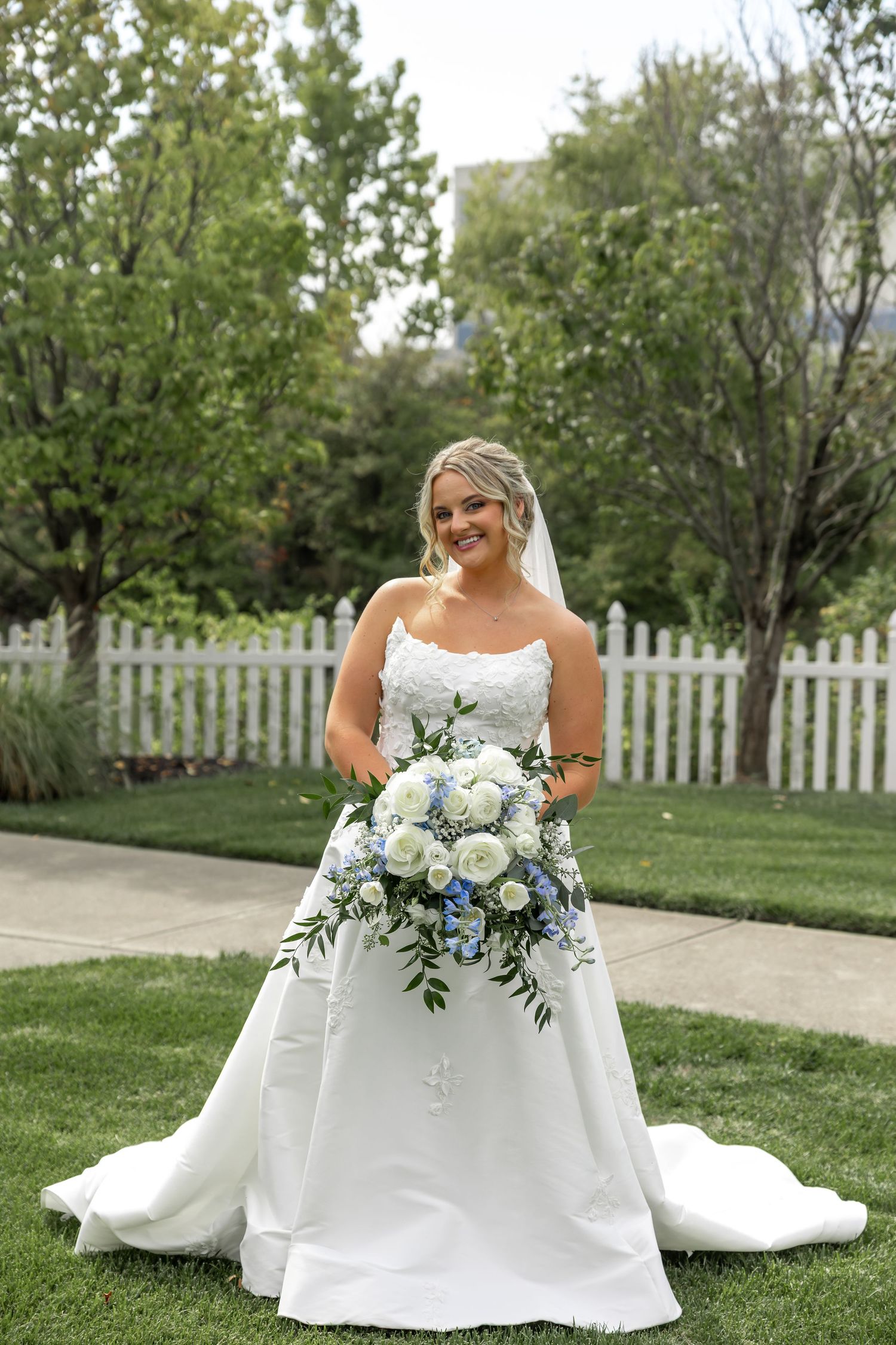 Elegant white wedding dress with blue floral bouquet arranged on green lawn.