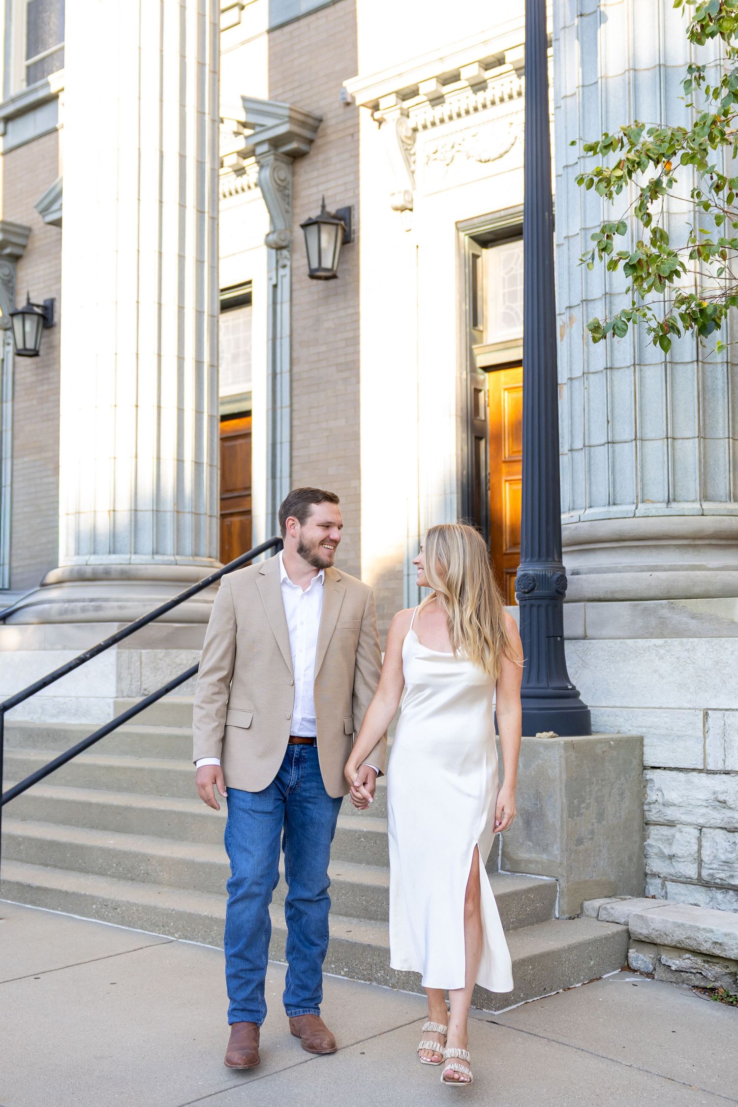 A couple poses on stone steps outside a historic building in formal attire.