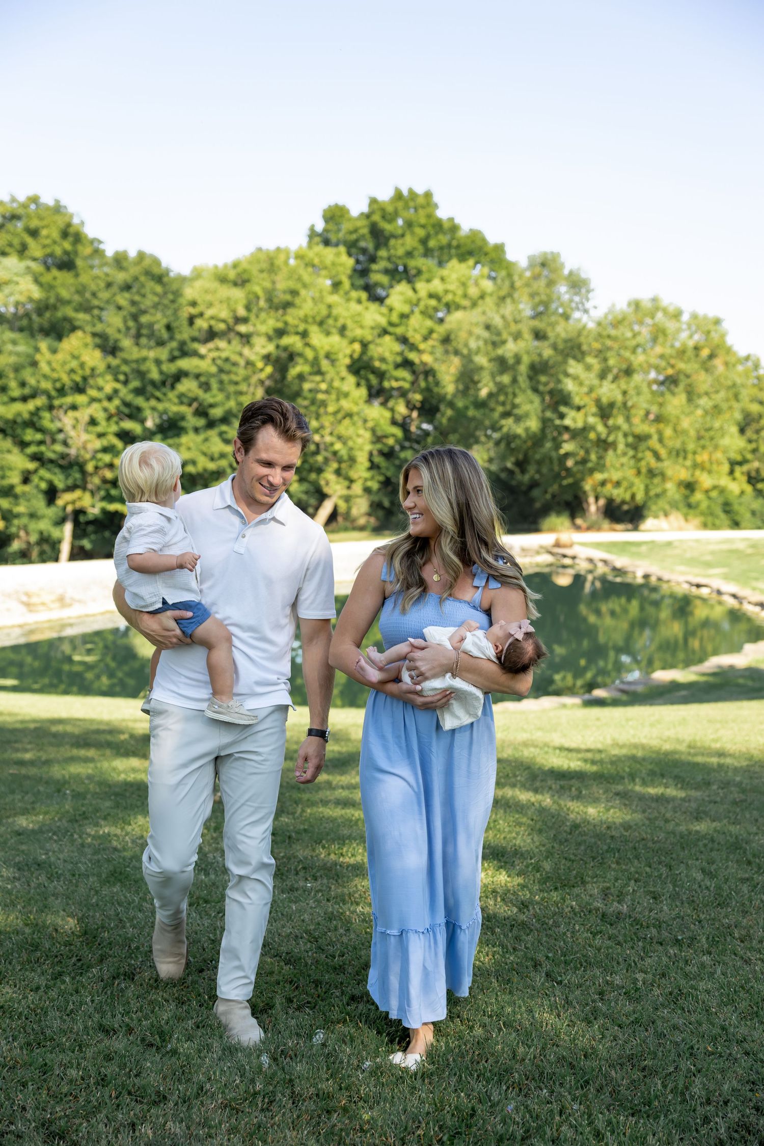 Family walking and playing together on a sunny grassy field in casual summer outfits.