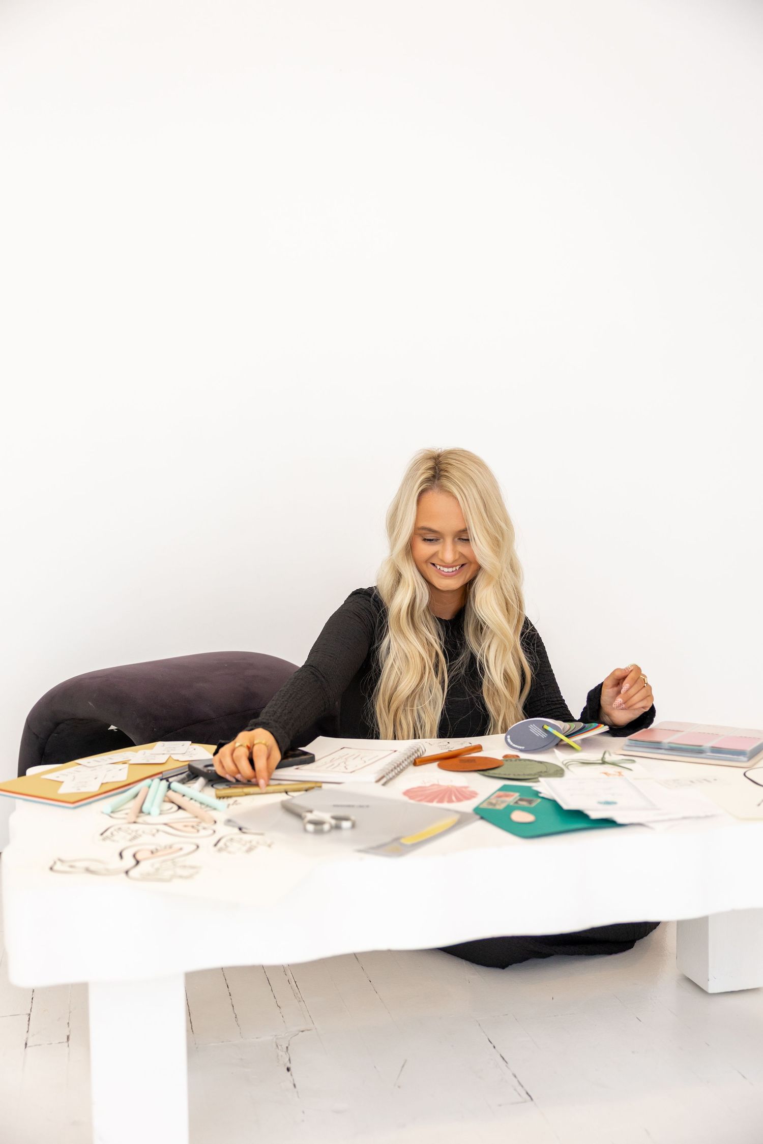 Person working at a white desk with various papers and materials spread out.