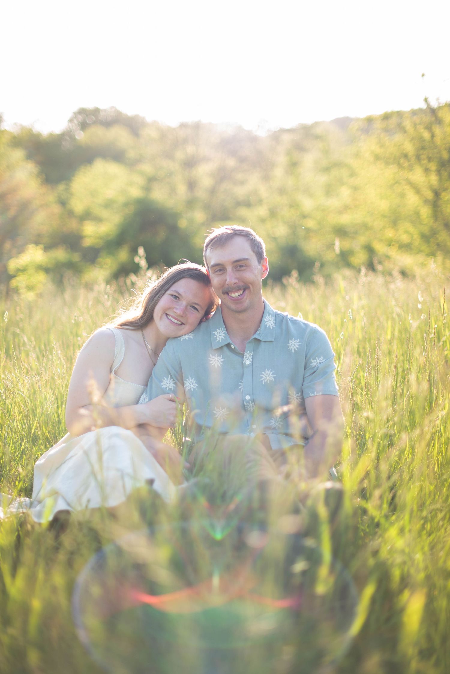 Couple sitting in a field in the mountains smiling at camera during portrait session