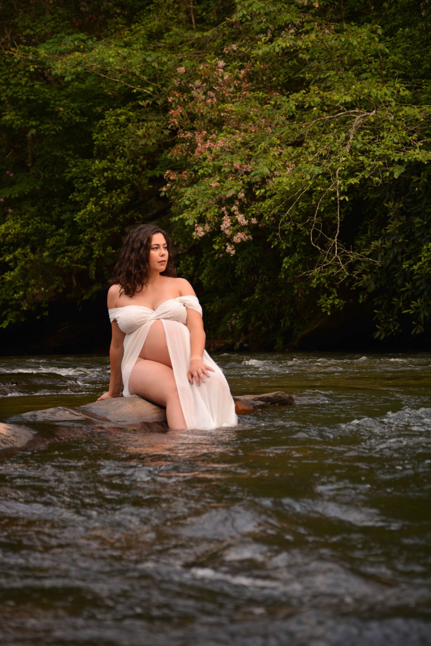 Pregnant woman sitting on a rock in the river in the spring for a lifestyle maternity session