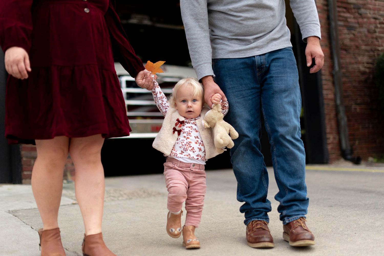 Toddler holding mom and dad's hands walking on sidewalk