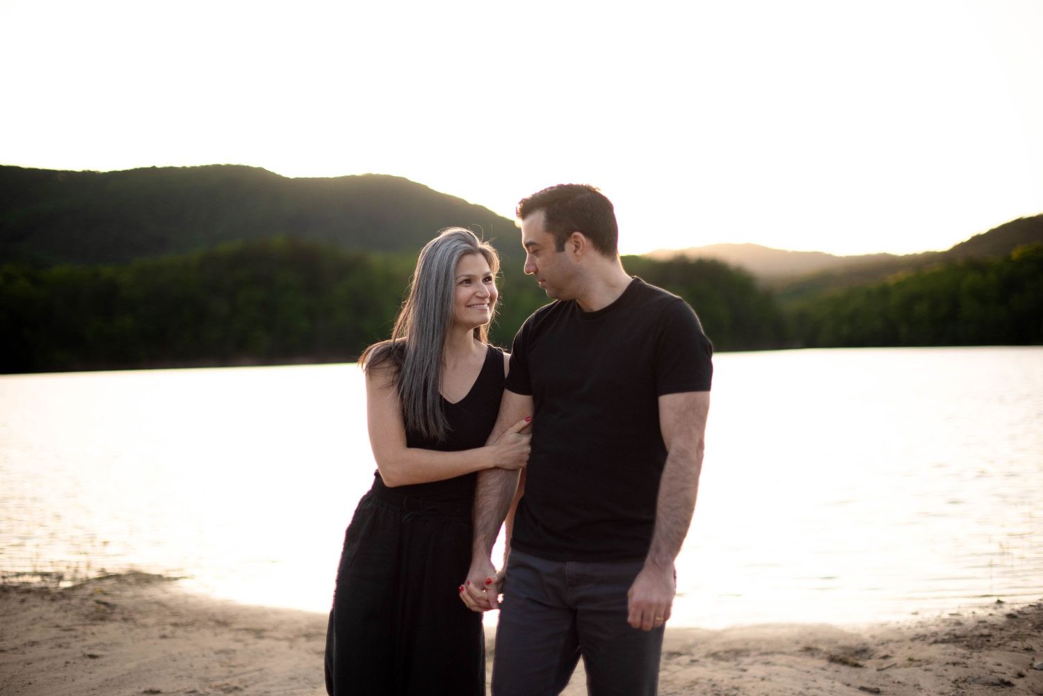 Couple holding hands walking beside lake in the mountains during portrait session