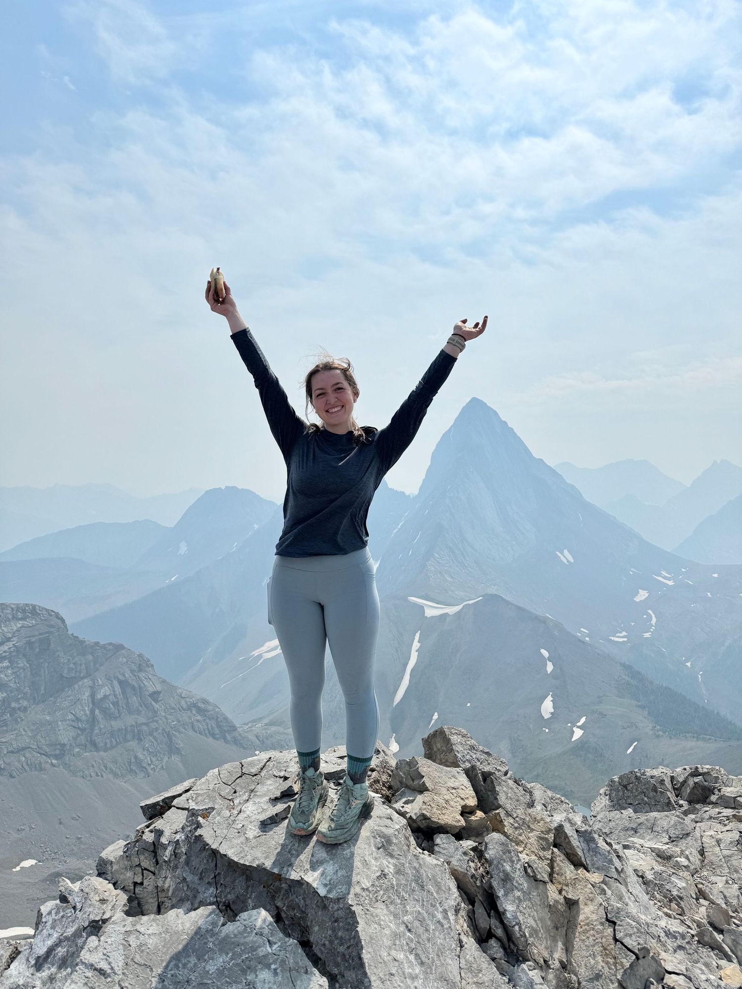 Photo of girl on top of mountain with hands raised.