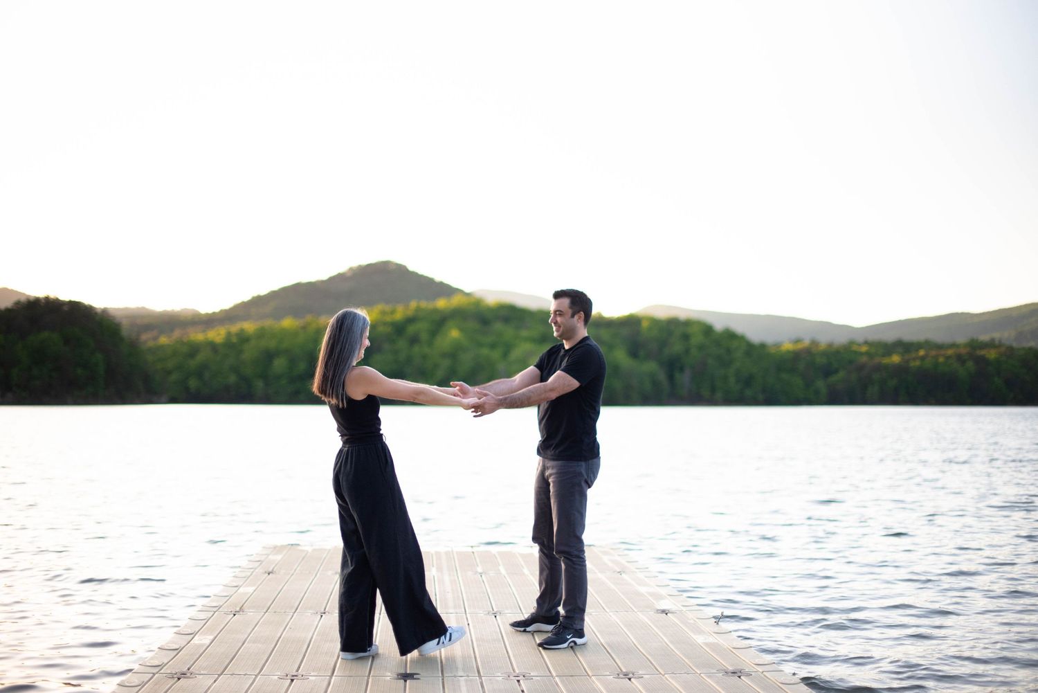Couple standing on dock with mountains in the background holding hands