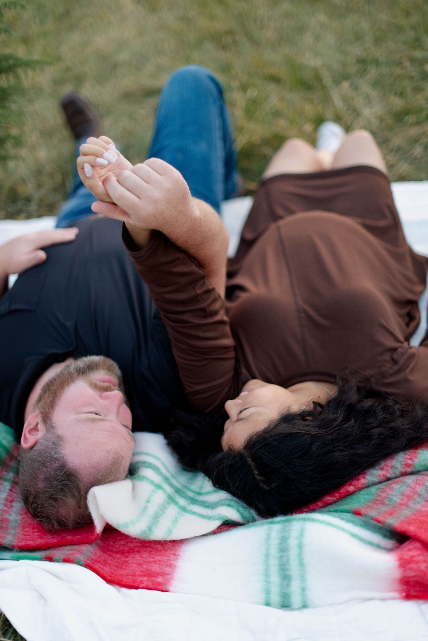 Parents laying on a blanket in a field laughing