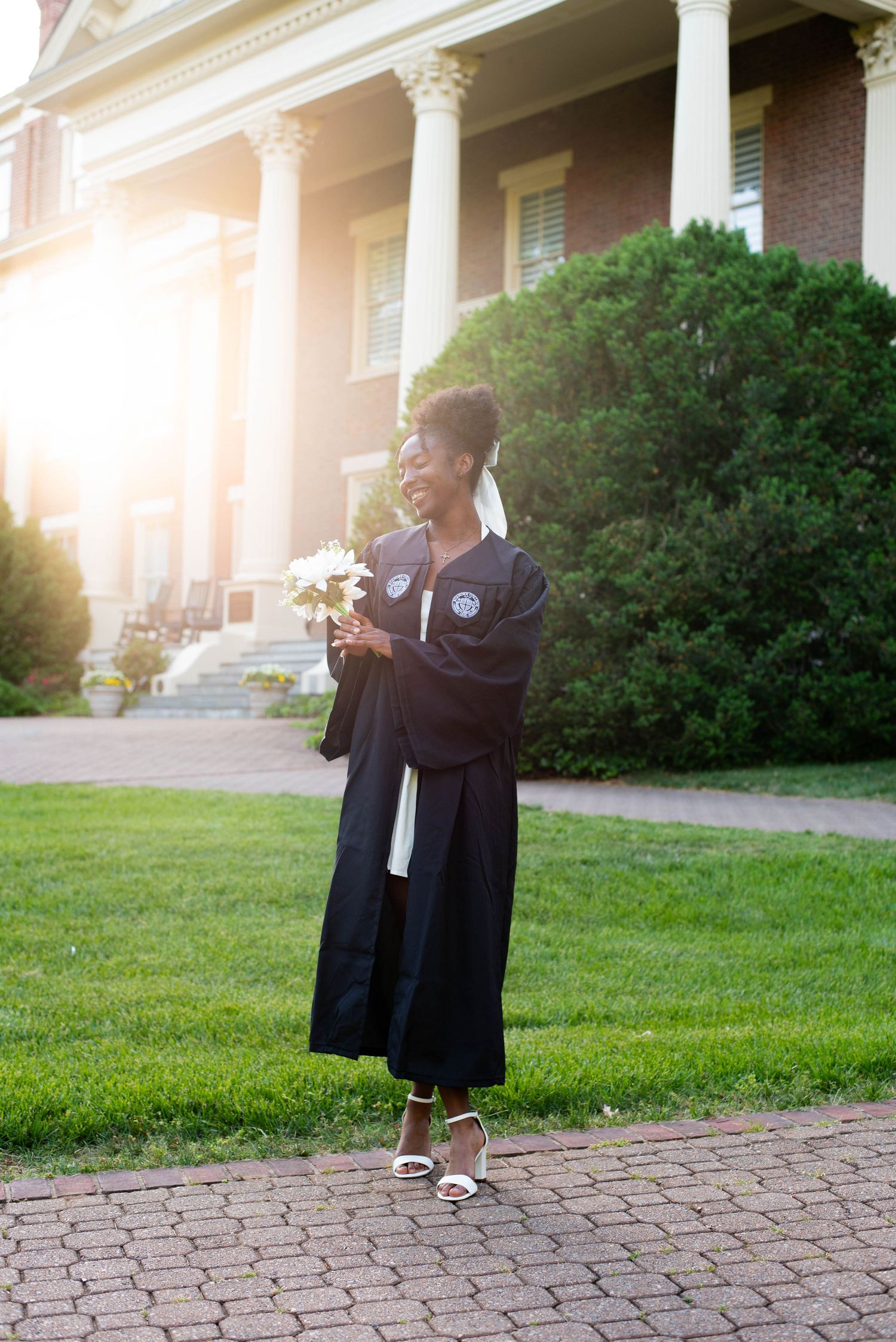 Senior graduation photos of a girl in her robe on campus holding flowers
