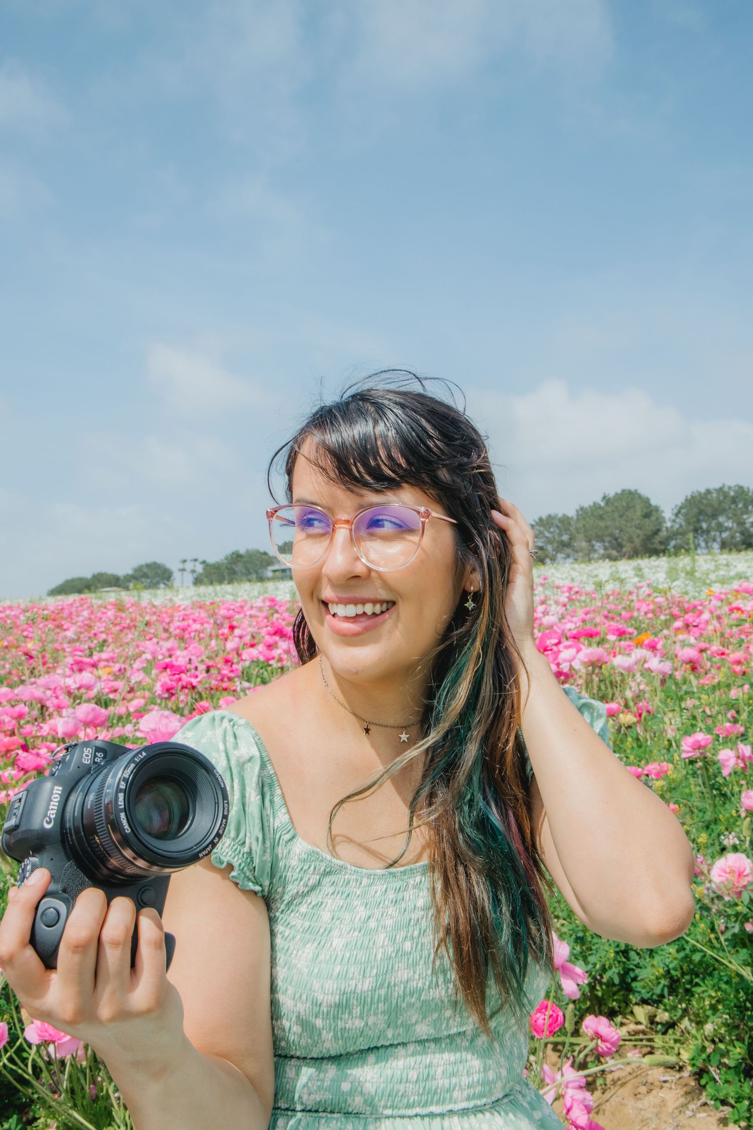 Kelsey Nevell sits in a flower field holding a camera and smiling.