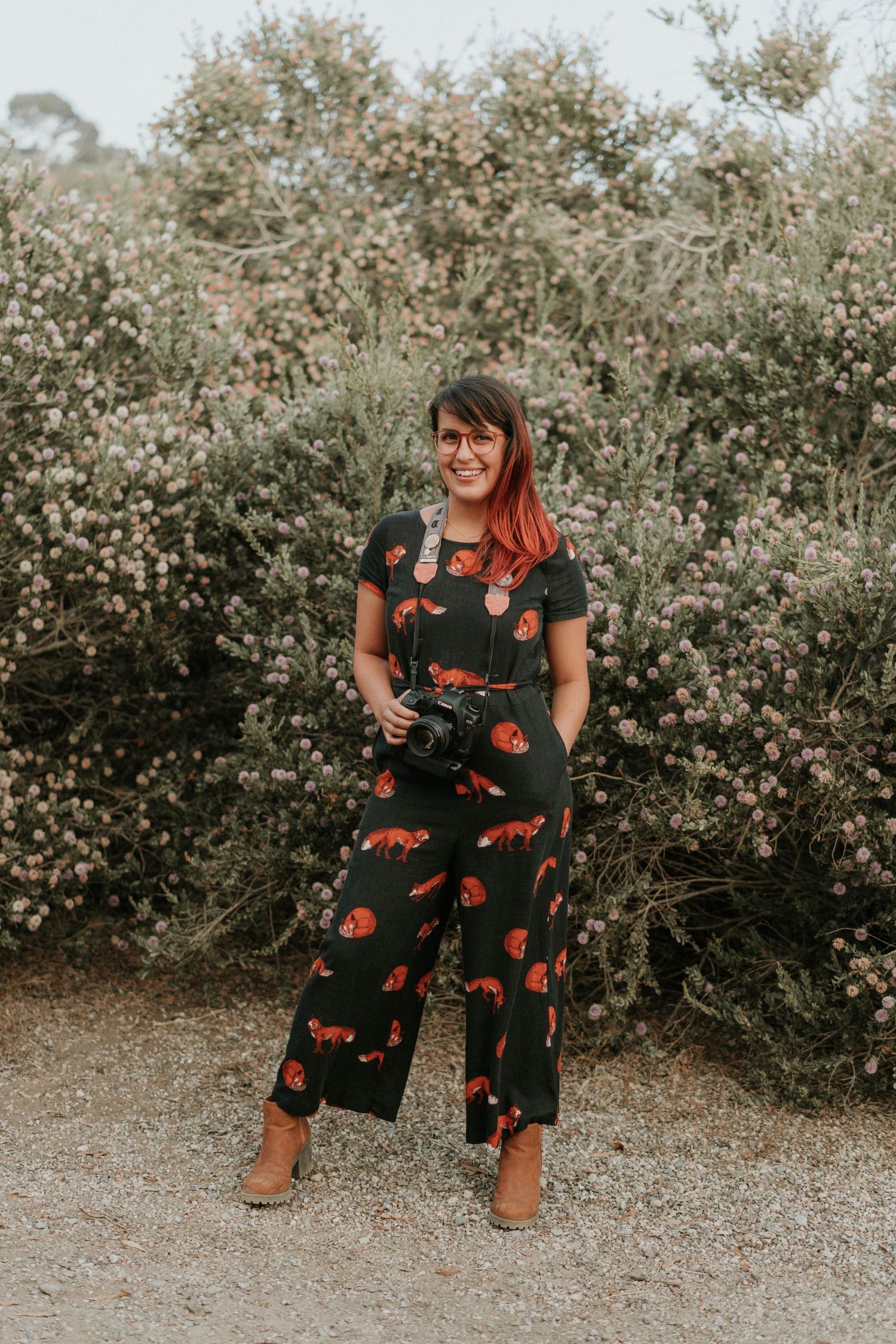 Kelsey Nevell stands with her camera in front of pink flowers in San Diego.