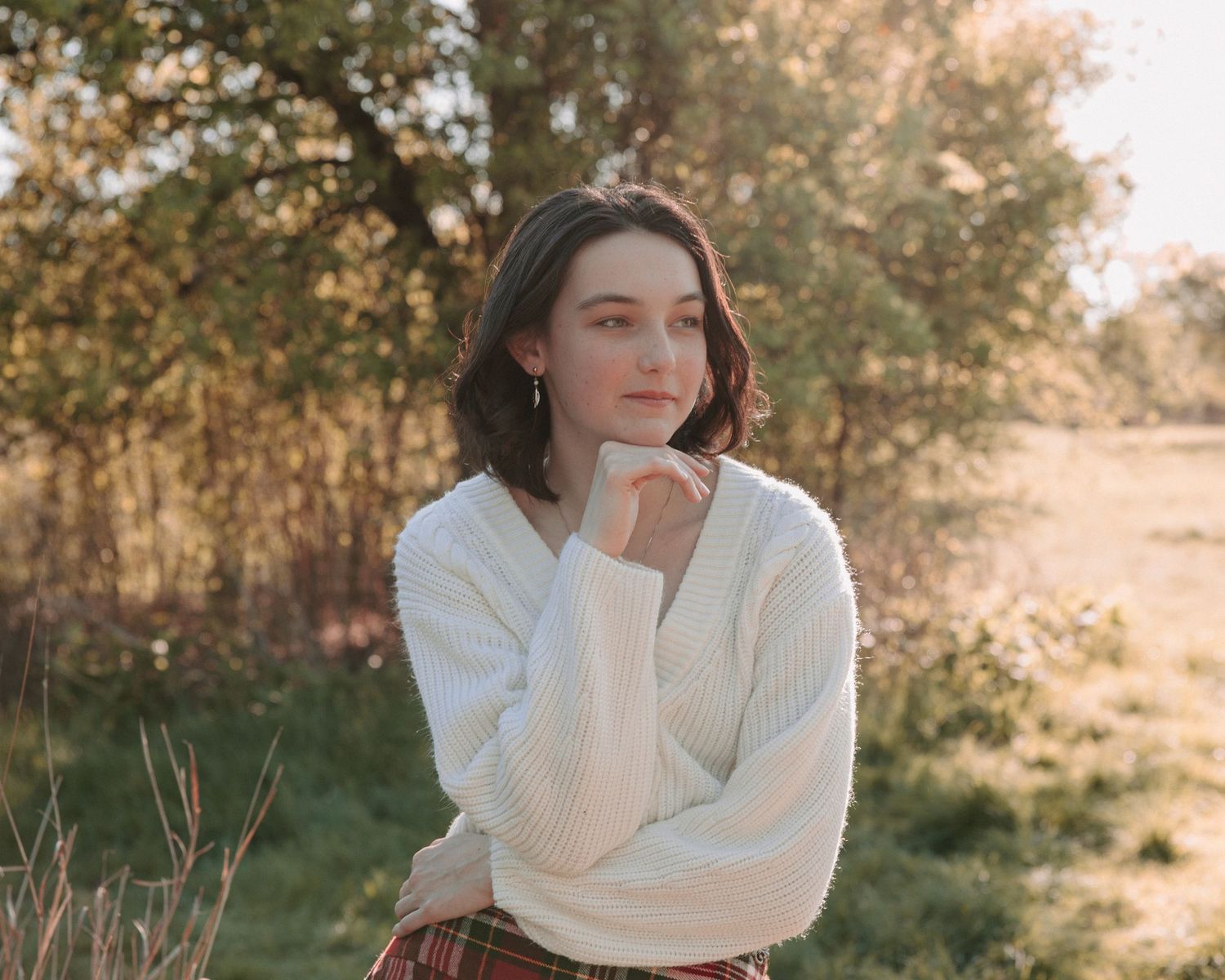 San Antonio Graduation. A person in a white sweater poses thoughtfully in an autumn field setting.