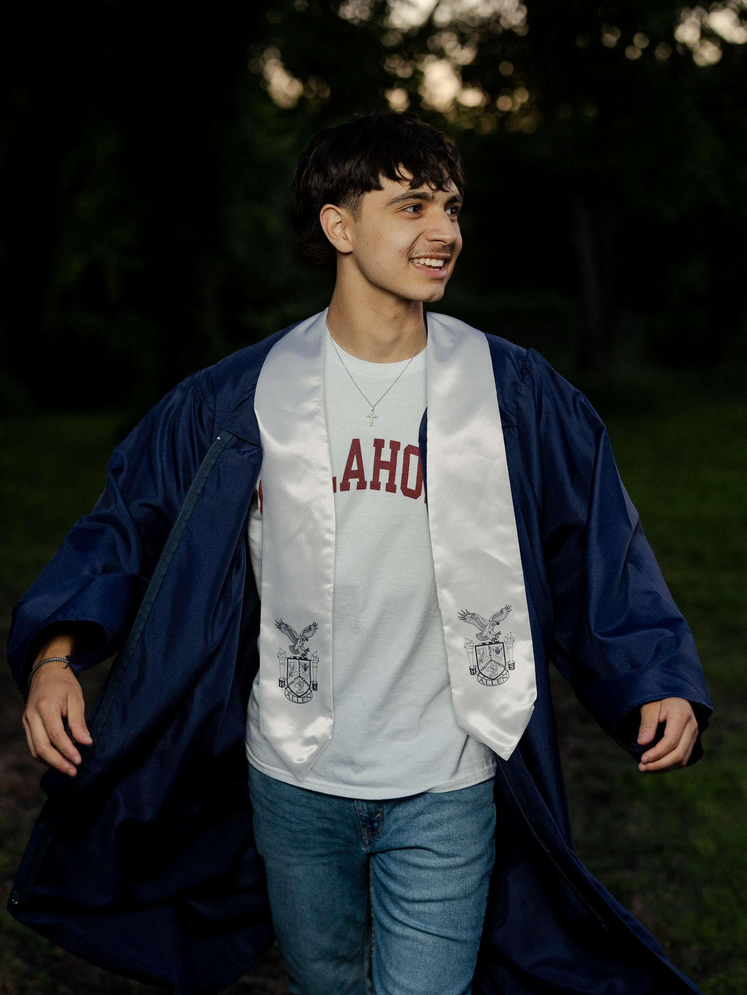 Young man in navy graduation gown and Idaho sash smiling outdoors, celebrating his academic achievement.