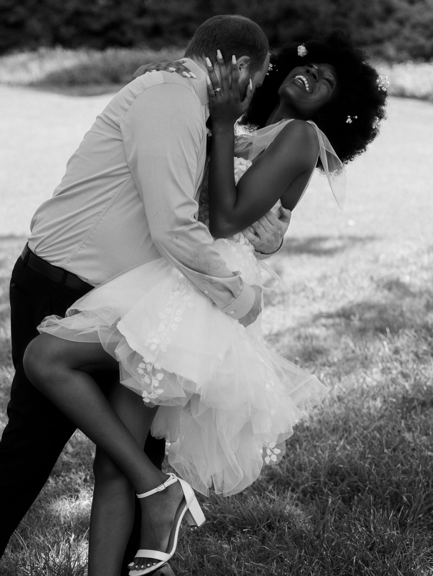 Romantic black and white photo of couple embracing in formal wedding attire outdoors.
