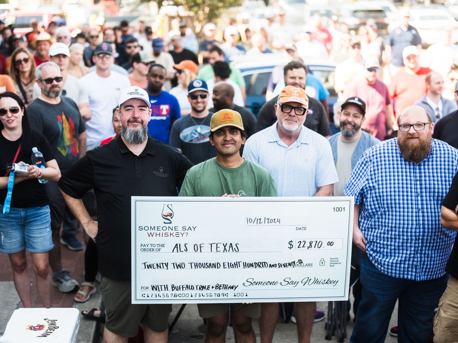 Group of men holding a large charity check for $22,810 made out to ALS of Texas at an outdoor event.