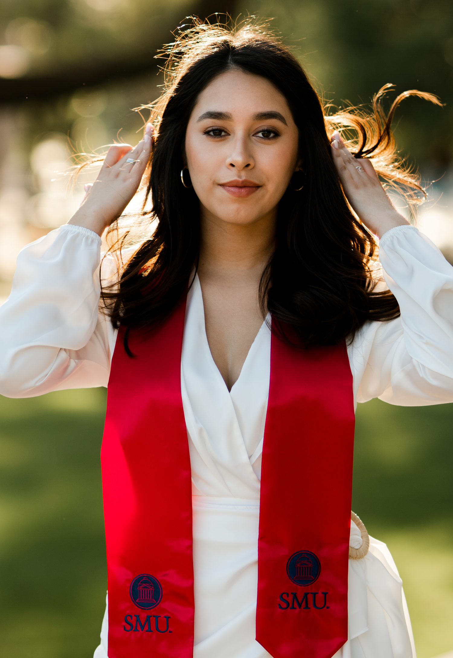Graduate in white blouse and red stole with SMU logo poses for portrait outdoors.