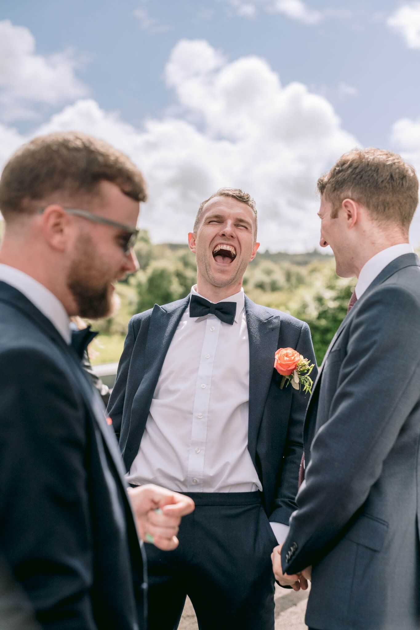Sequence of joyful candid moments between groomsmen in formal suits at an outdoor wedding.