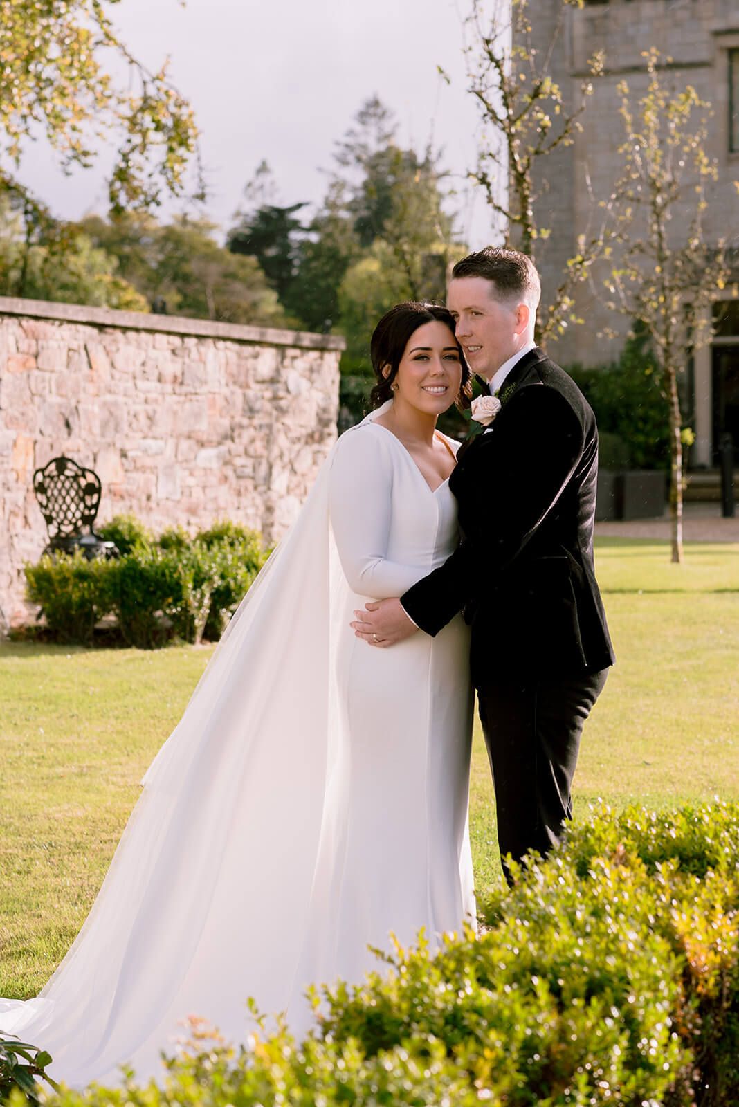 A tender moment captured between newlyweds in front of a stone wall in a garden setting.