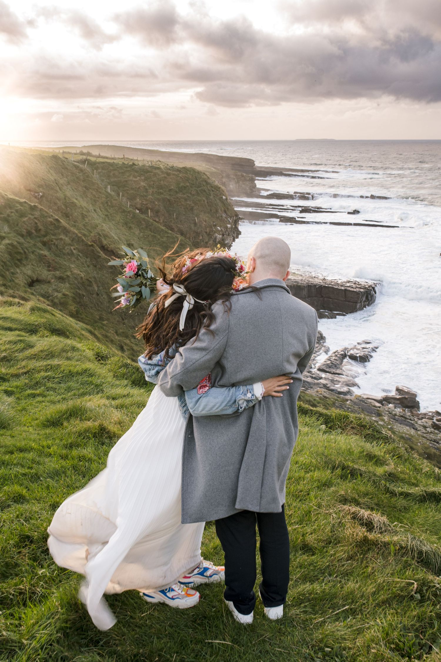 Couple embracing on dramatic coastal cliffs at sunset overlooking the ocean.
