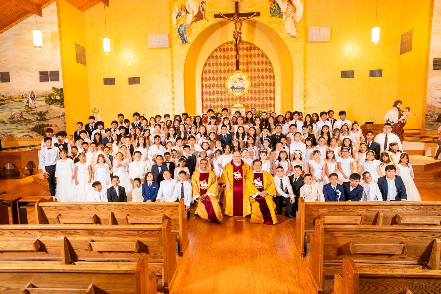 Large group of children and adults in formal attire posing inside a decorated Catholic church during a confirmation ceremony.