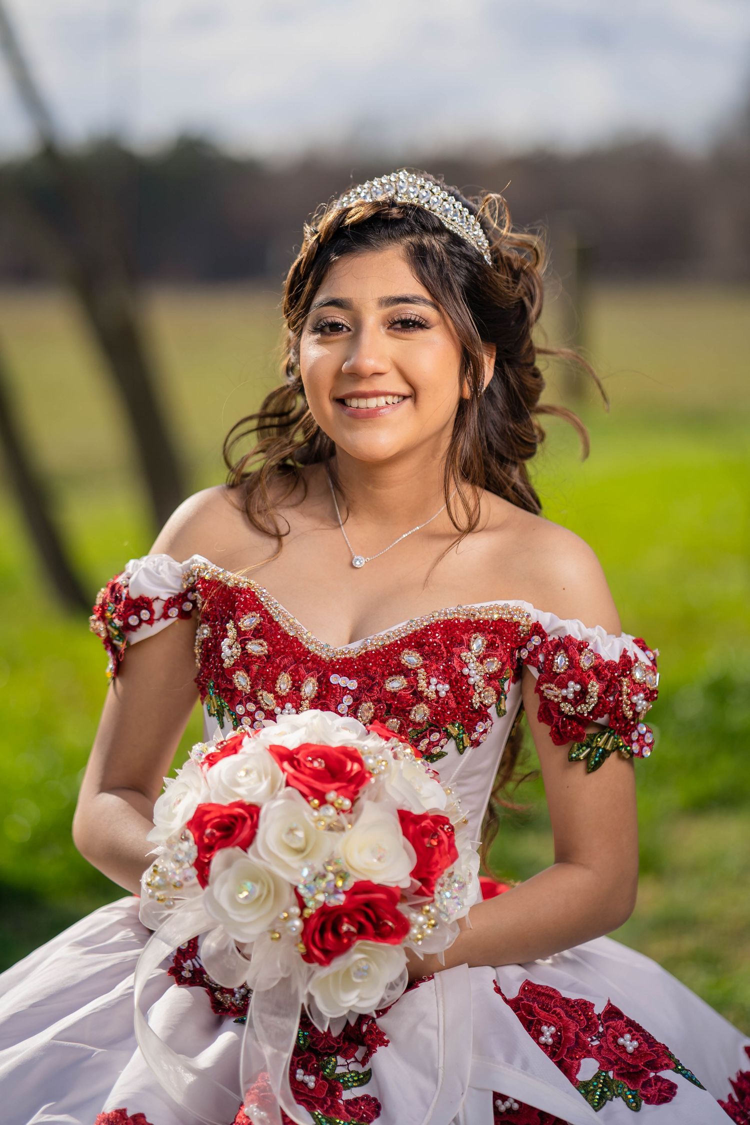 Elegant quinceanera celebration featuring a white and red themed dress with floral details in an outdoor setting.