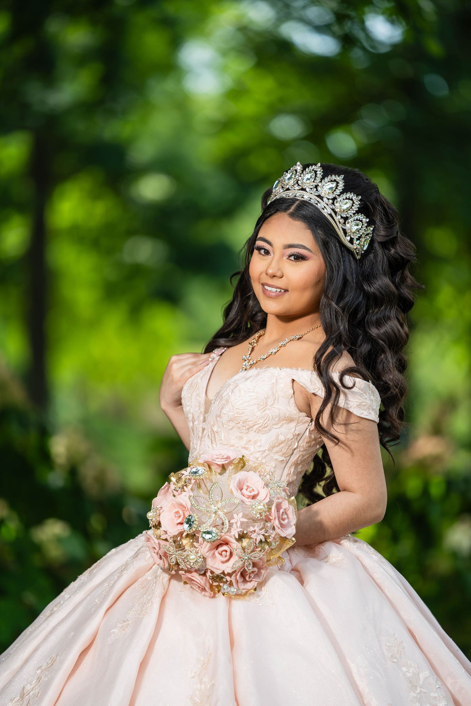 A person in a peach-colored quinceañera ball gown with lace details poses outdoors against a green natural backdrop.