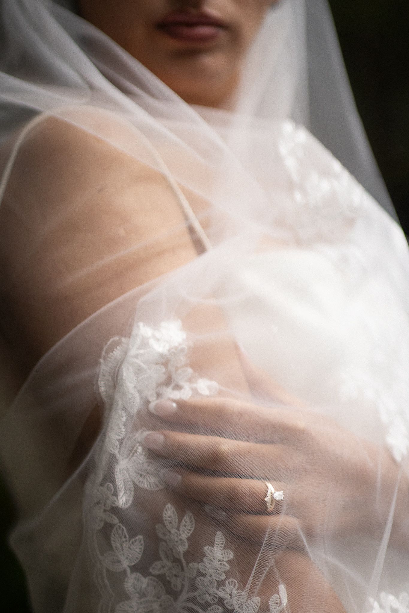 Sharp focus on the bride's wedding rings on her hand, through her bridal veil.