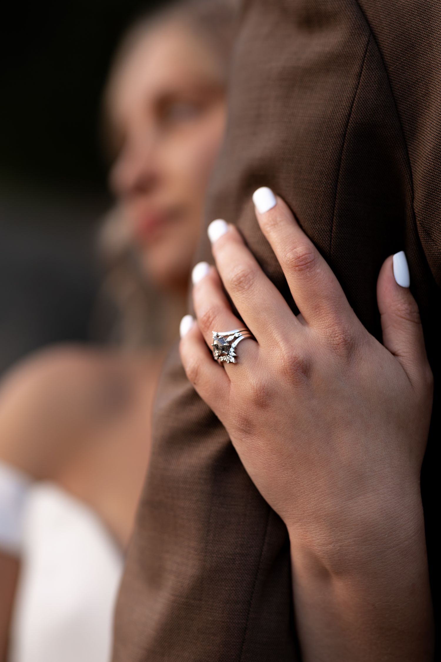 Sharp focus on a custom salt and pepper diamond wedding set on an eloping brides hand, holding her husband's arm. Moody edit with true color